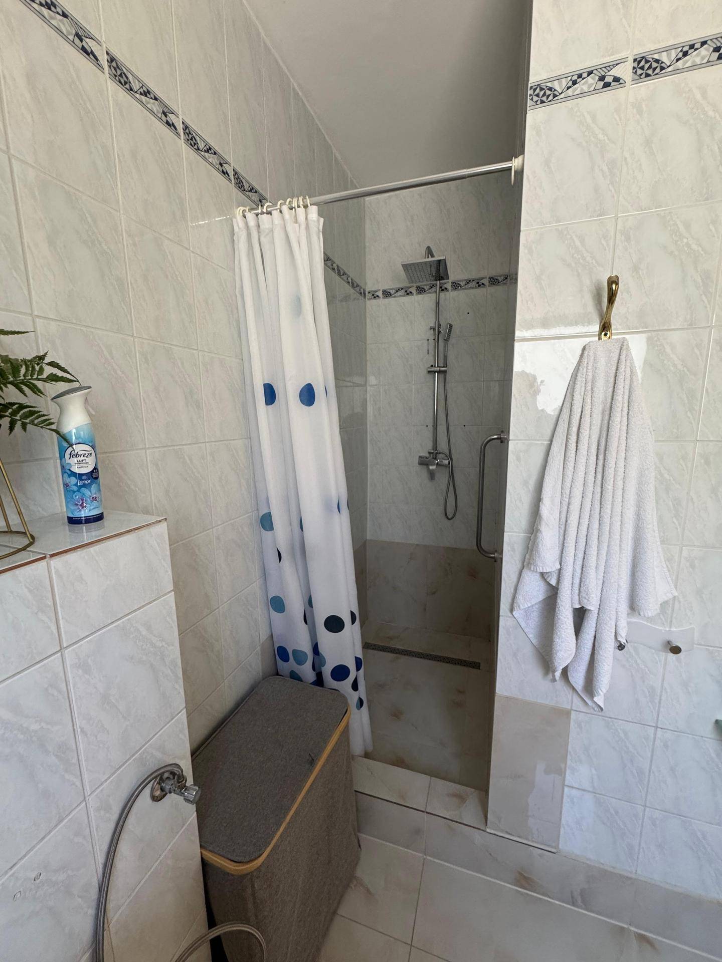 Duschbereich im Badezimmer mit Regendusche und Duschvorhang, umgeben von hellen Fliesen.