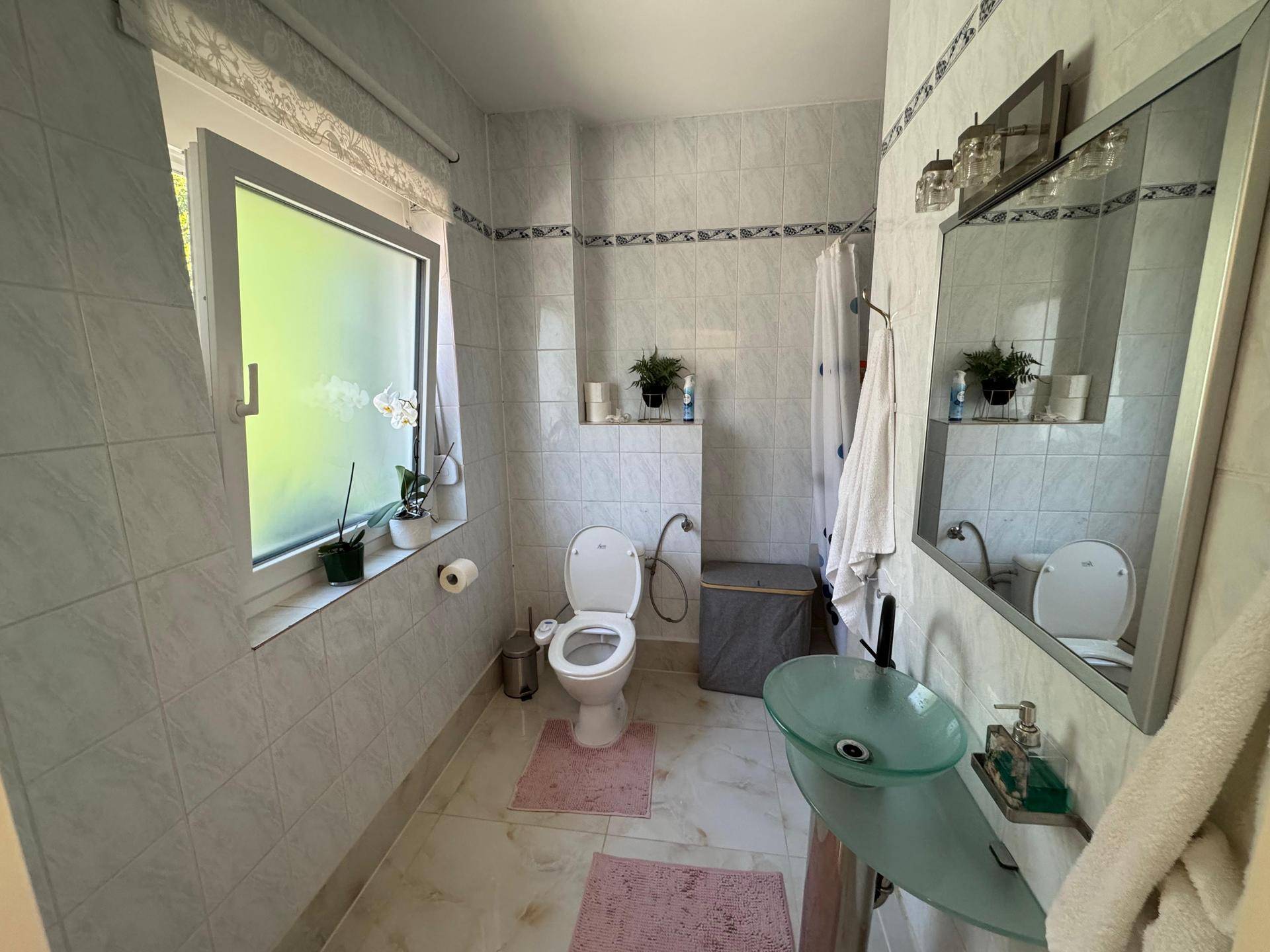 Helles Badezimmer mit WC, modernem Waschbecken und Fenster, ausgestattet mit hellen Fliesen.
