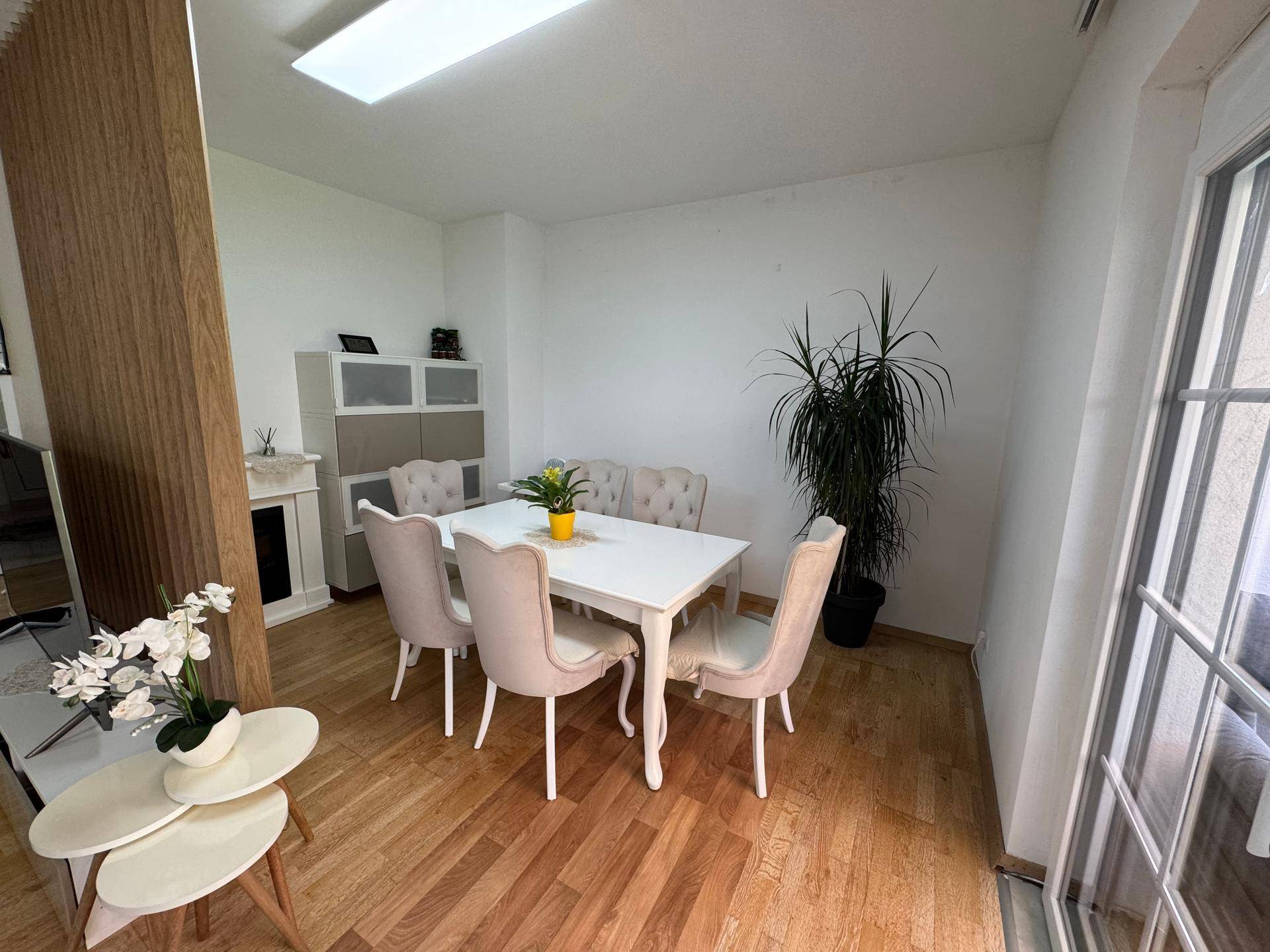Heller Essbereich mit Holzboden, weißem Esstisch und bequemen Stühlen, offen zum Wohnzimmer.