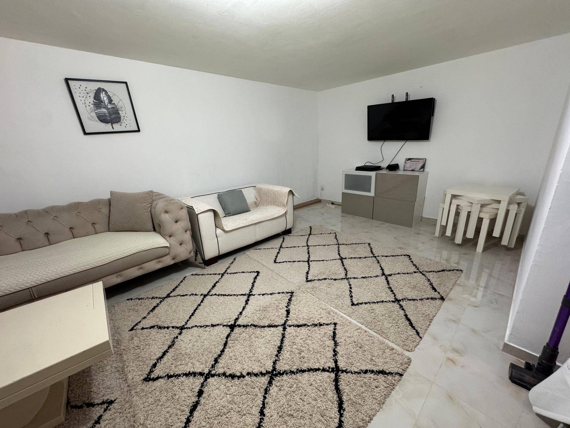 Wohnzimmer mit Wandfernseher, bequemen Sofas und einem großen Teppich, der den Raum gemütlich macht.