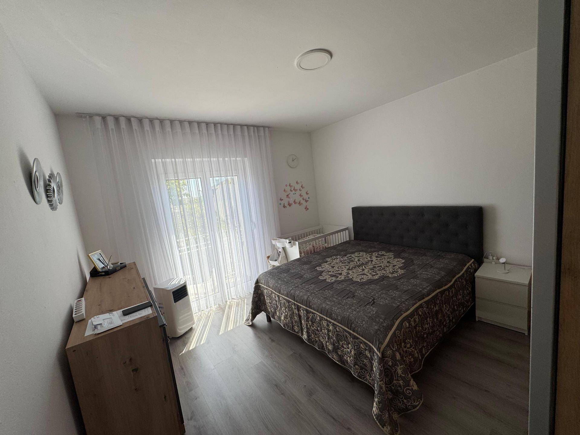 Helles Schlafzimmer mit Doppelbett, Laminatboden und Zugang zu einem französischen Balkon.