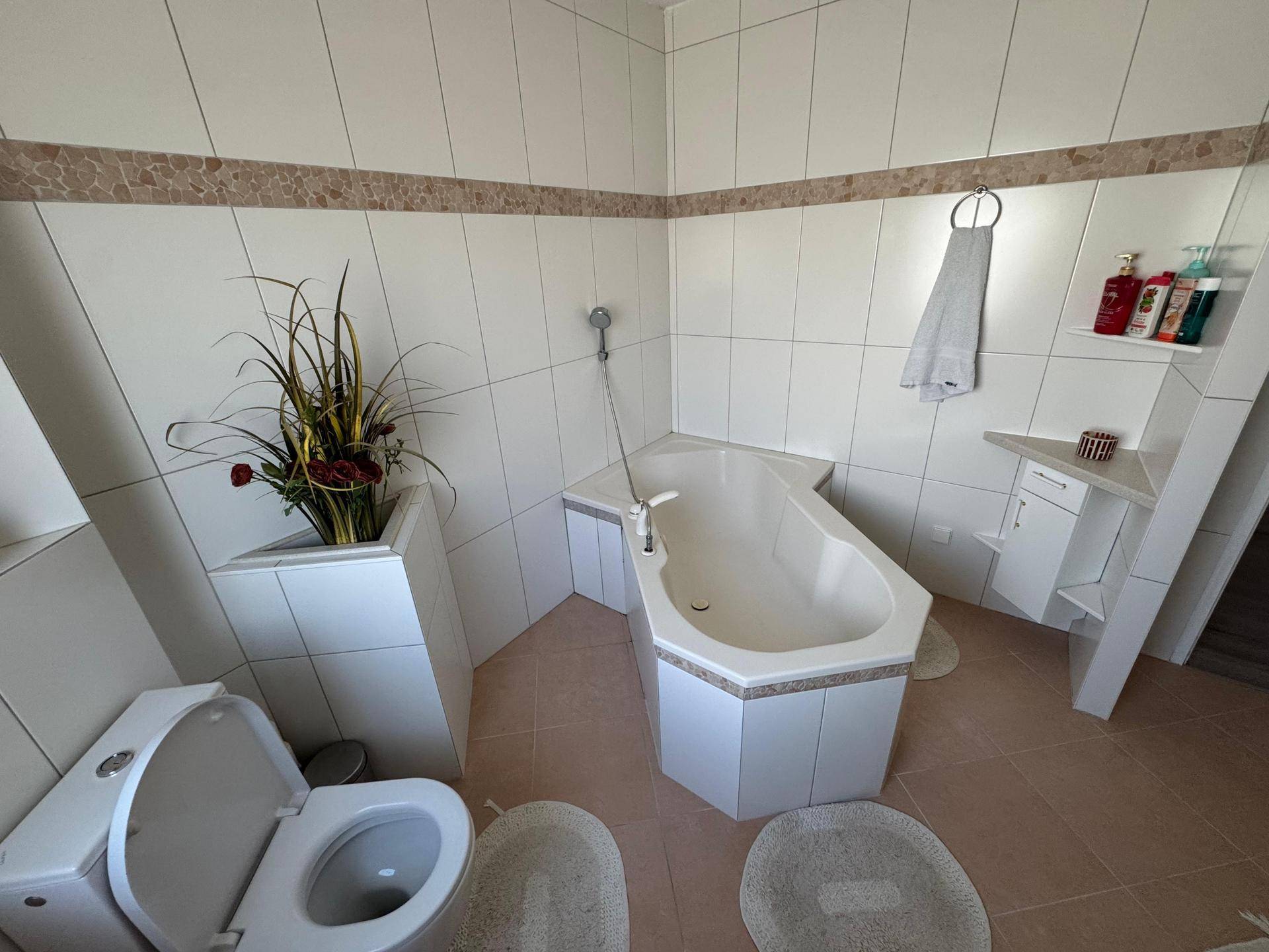 Badezimmer mit Eckbadewanne und Toilette, ausgestattet mit hellen Fliesen und dekorativen Akzenten.