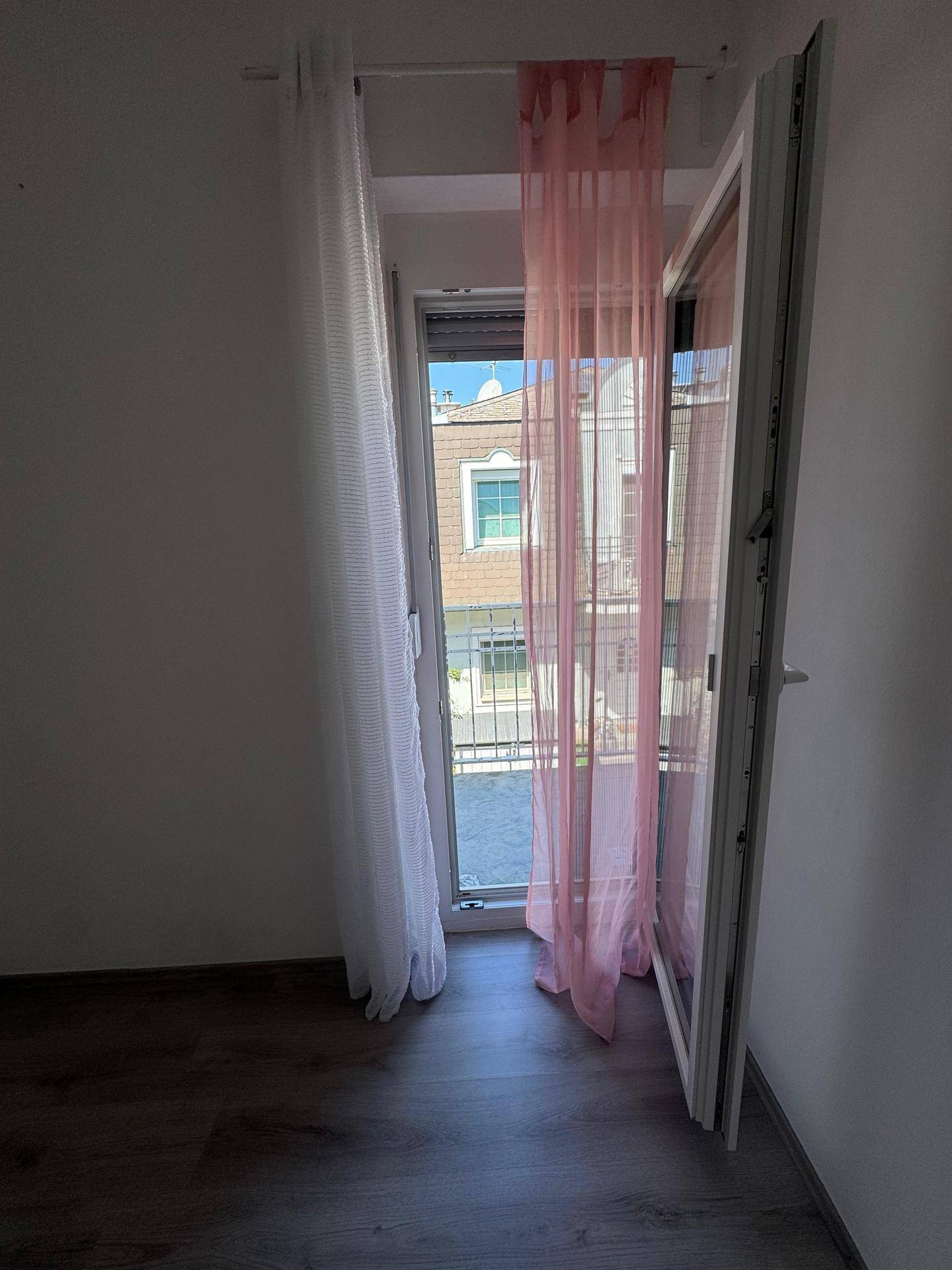 Offenes Fenster mit rosa und weißen Vorhängen, das einen Blick auf die Nachbarschaft bietet.