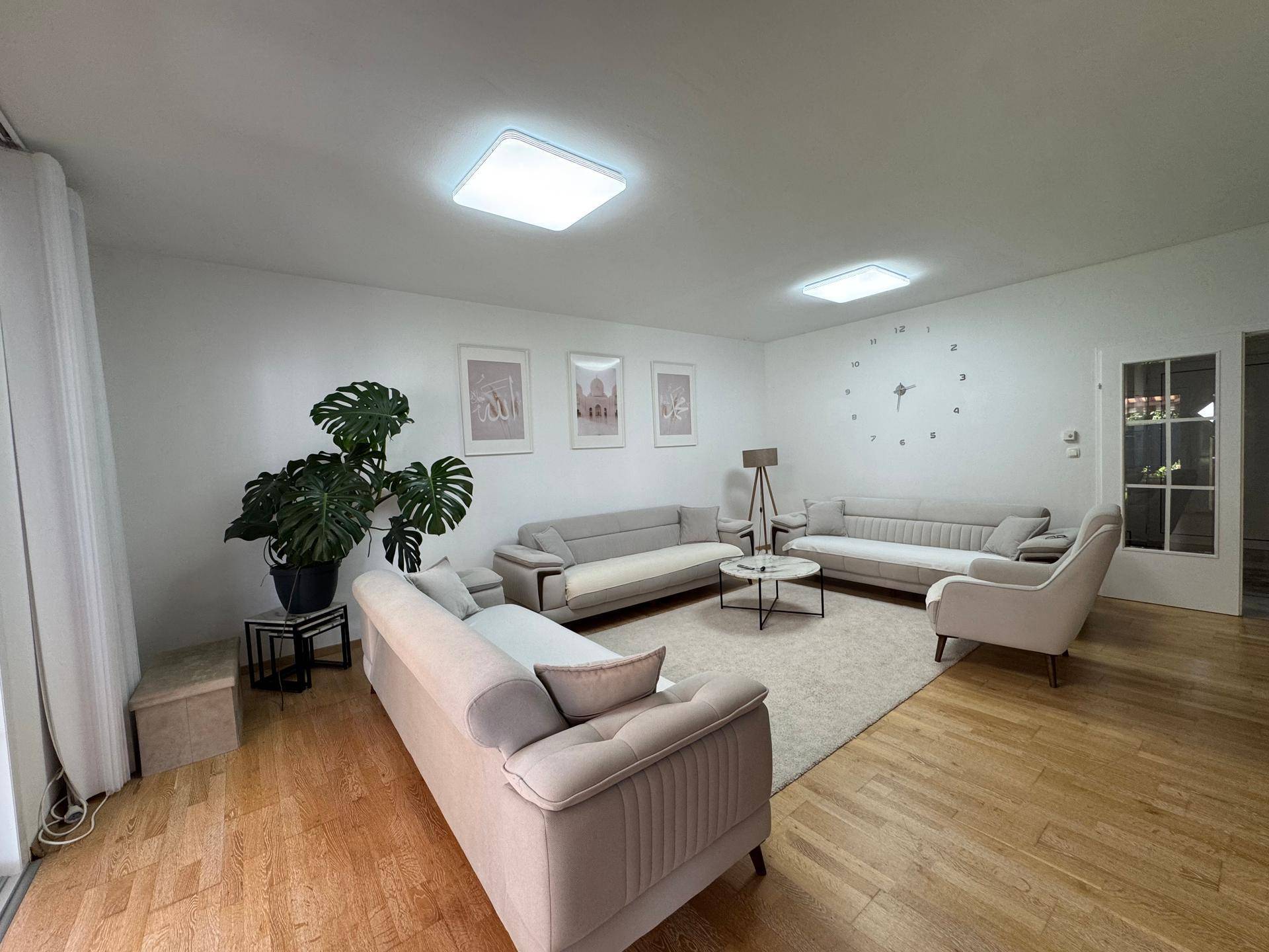 Helles Wohnzimmer mit modernem Mobiliar, Holzboden und dekorativer Wanduhr, ideal zum Entspannen.