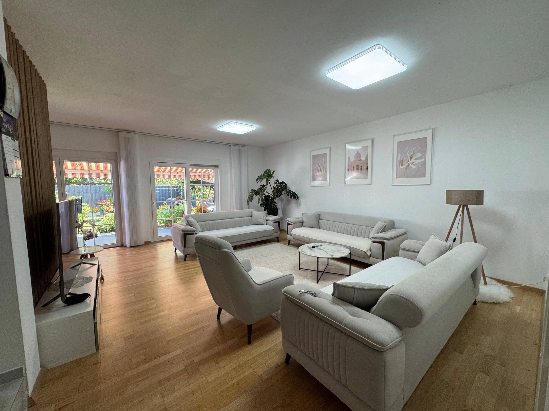 Geräumiges Wohnzimmer mit hellem Holzboden, bequemen Sofas und Zugang zur Terrasse und Garten.