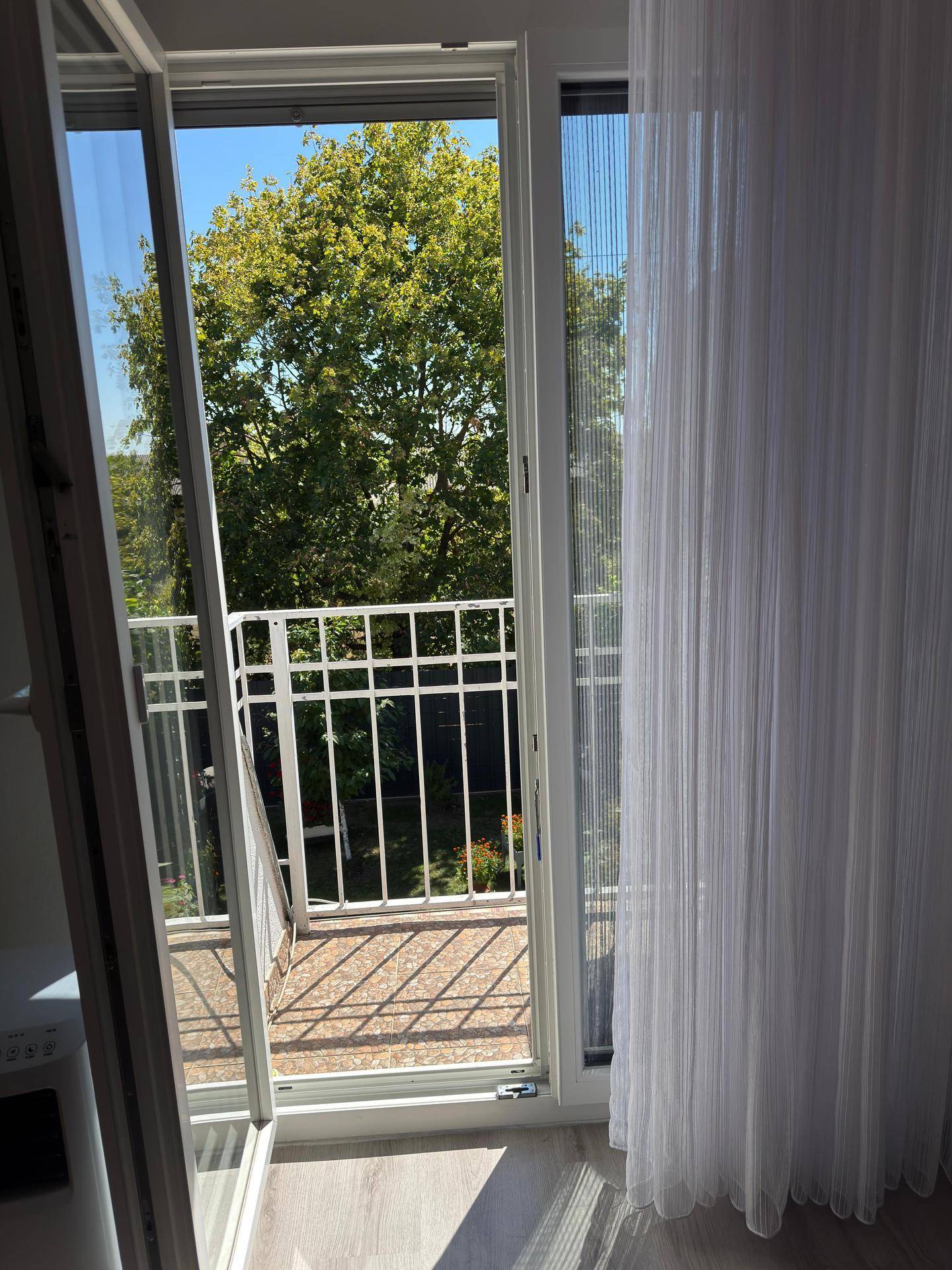 Blick aus dem Schlafzimmer auf den grünen Baum und den französischen Balkon mit Geländer.