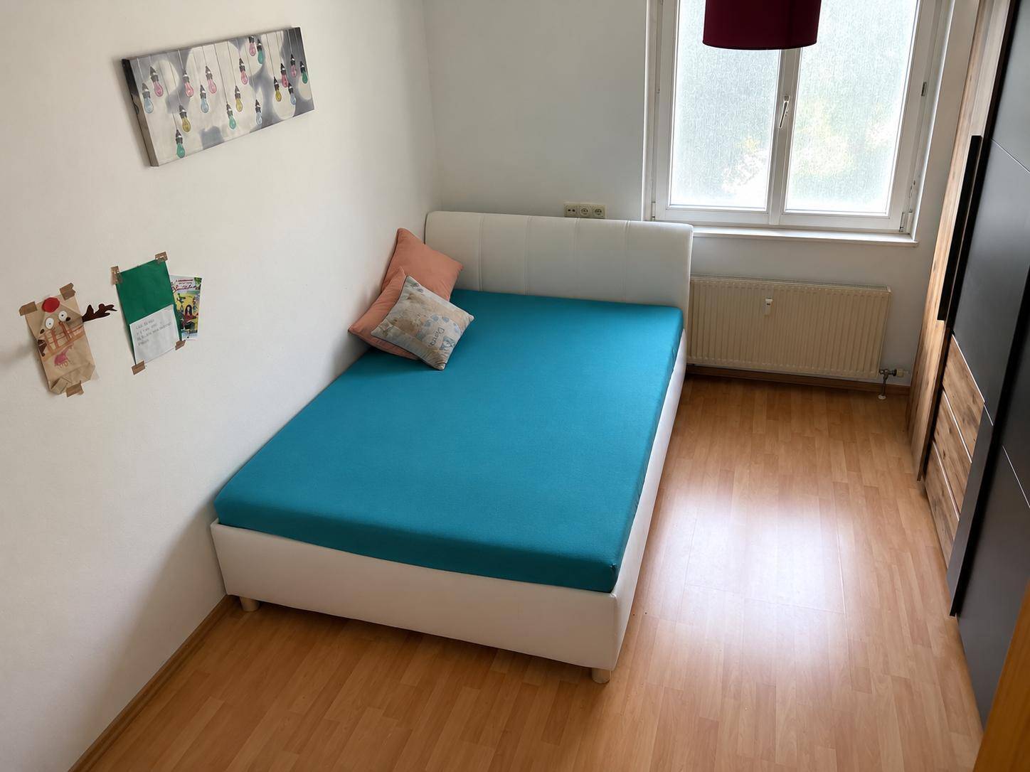 Helles Schlafzimmer mit Einzelbett, Fenster und hellem Laminatboden.