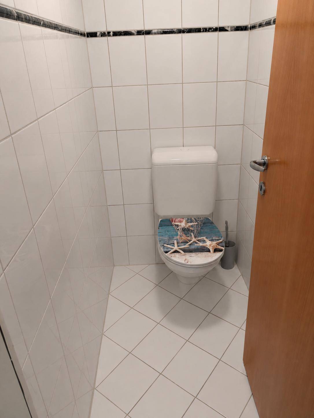Kleines WC mit Toilette, weißen Fliesen und dekorativem Toilettendeckel.
