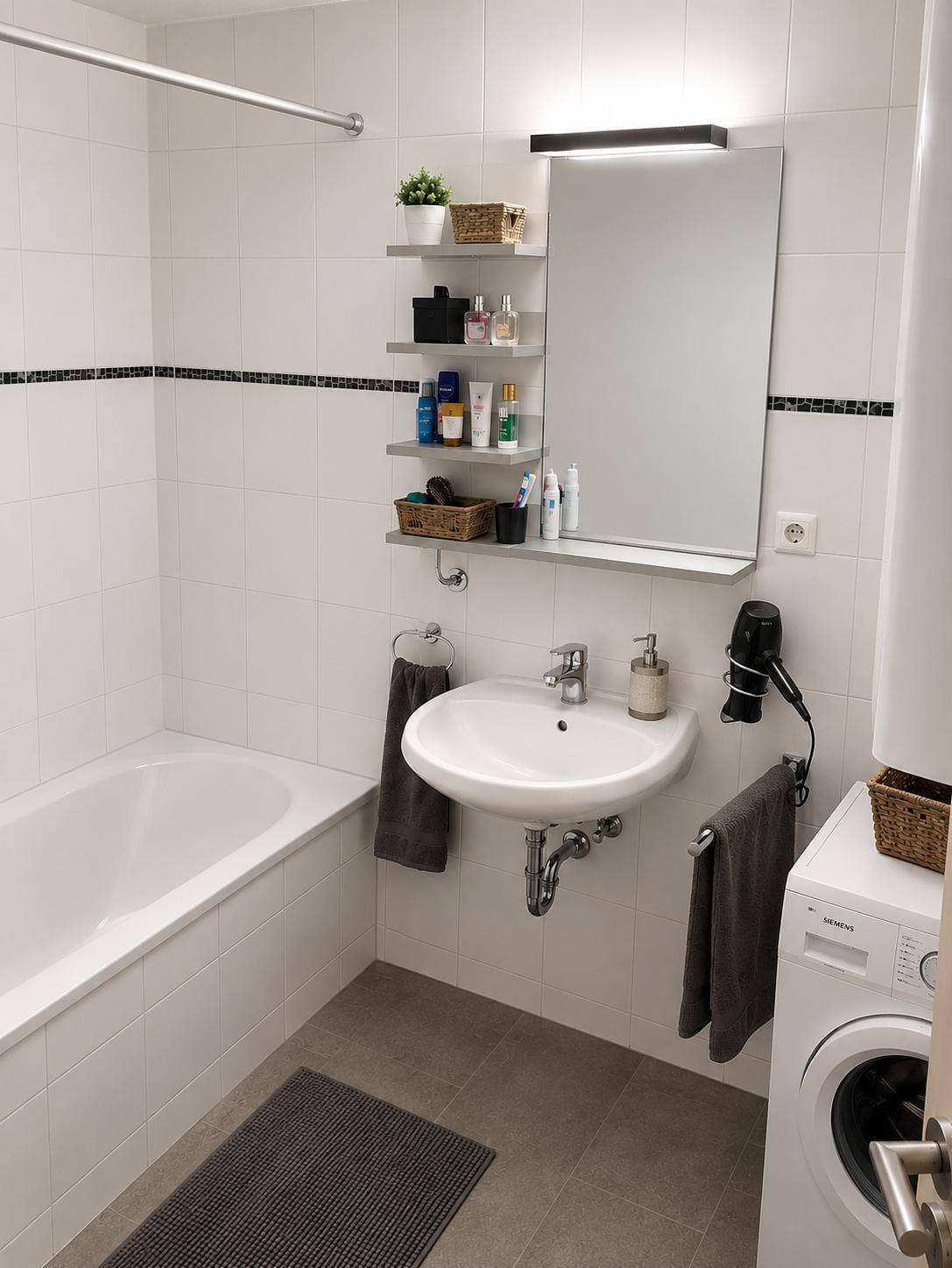 Helles Badezimmer mit Badewanne, Waschbecken, Spiegelschrank und Waschmaschine.
