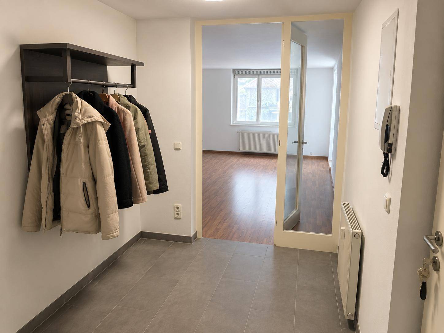 Eingangsbereich mit Garderobe und grauen Fliesen, der in einen hellen Wohnbereich führt.