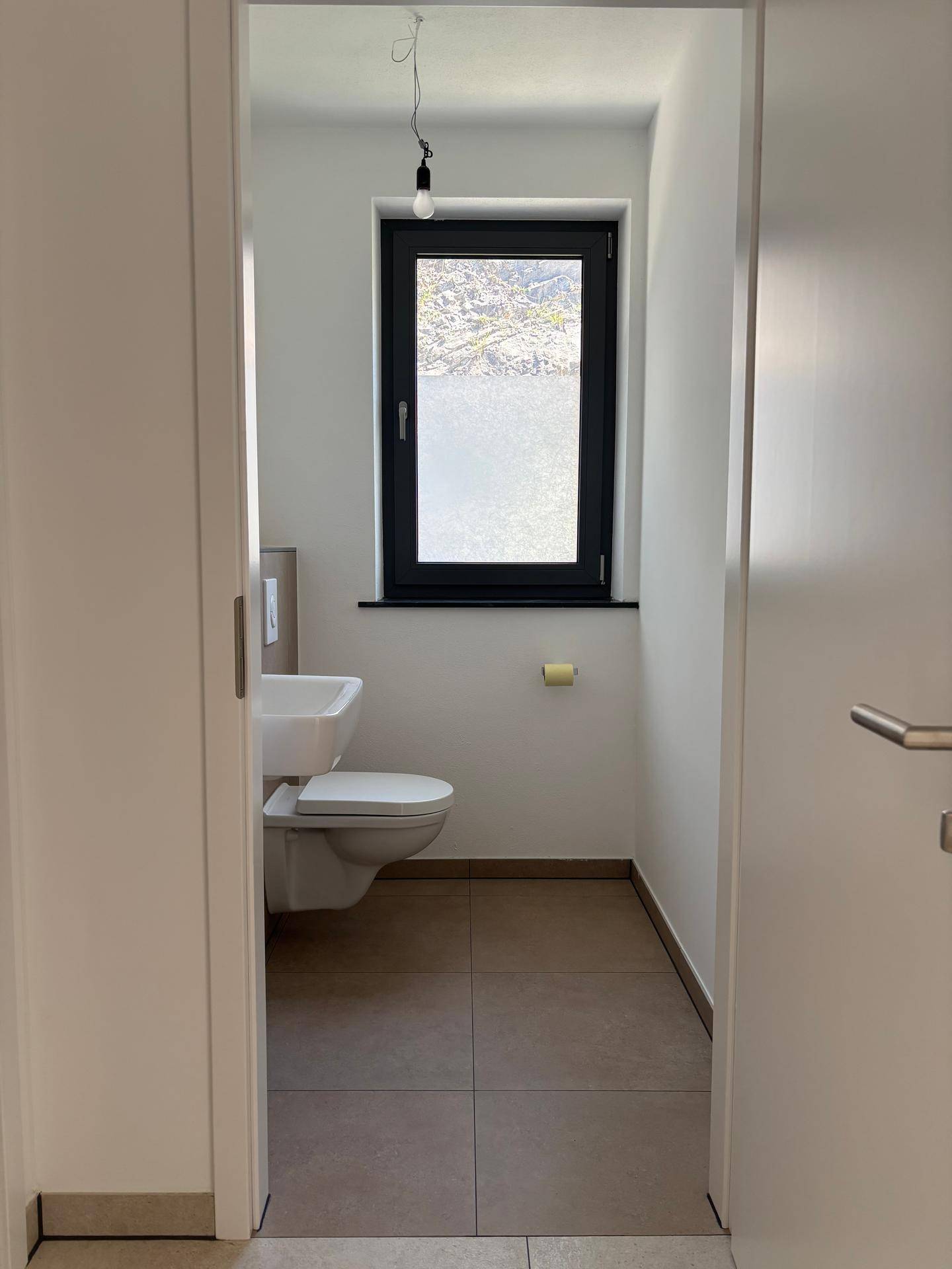 Helles Gäste-WC mit wandhängender Toilette, kleinem Waschbecken und Fenster.