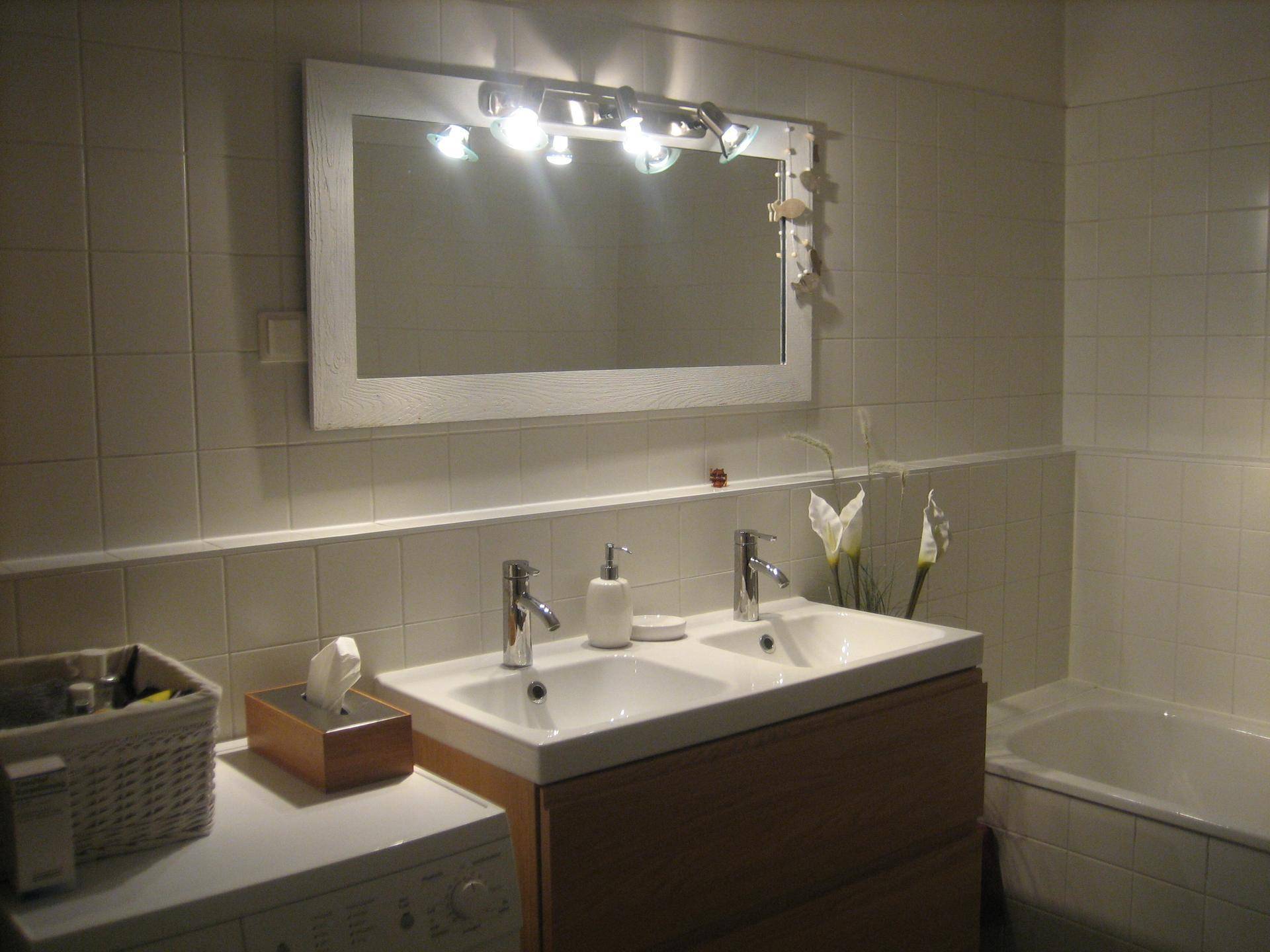Helles Badezimmer mit Doppelwaschbecken, großem Spiegel, Badewanne und weißen Fliesen.
