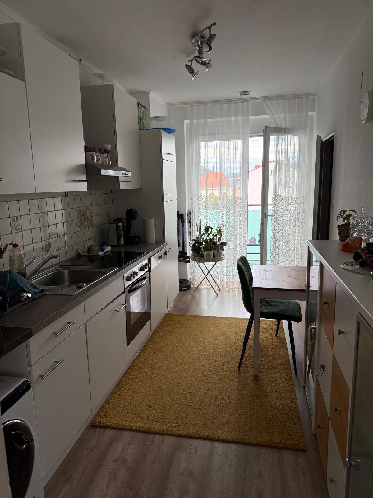 Schmale Küche mit weißen Einbauschränken, Essbereich und Zugang zum Balkon.