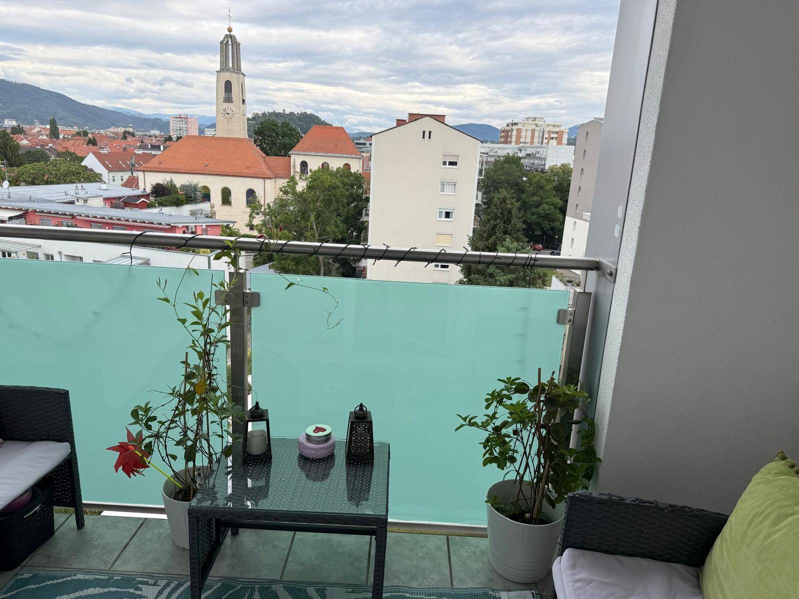 Balkon mit Sitzgelegenheiten und weitem Blick über die Stadt und eine Kirche.