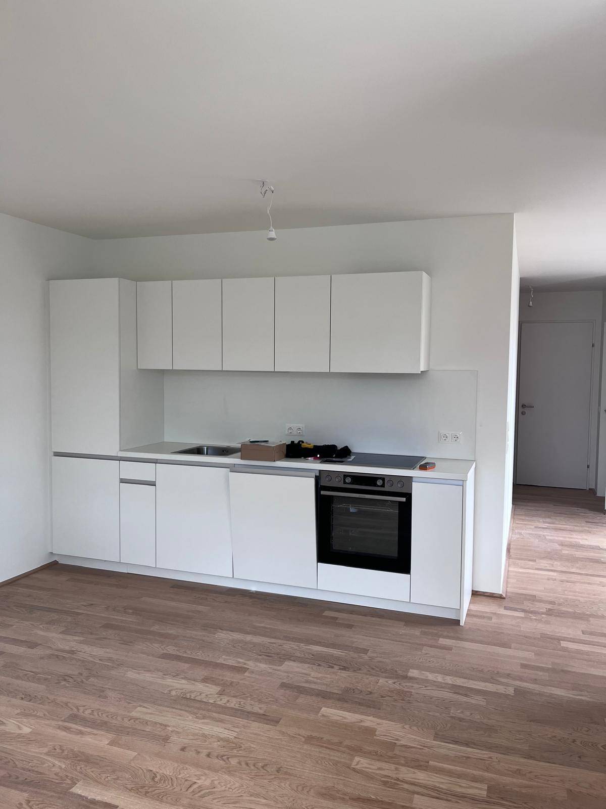 Vollständige Ansicht der neuen Einbauküche mit weißen Fronten, Spüle und modernen Geräten auf Holzboden.