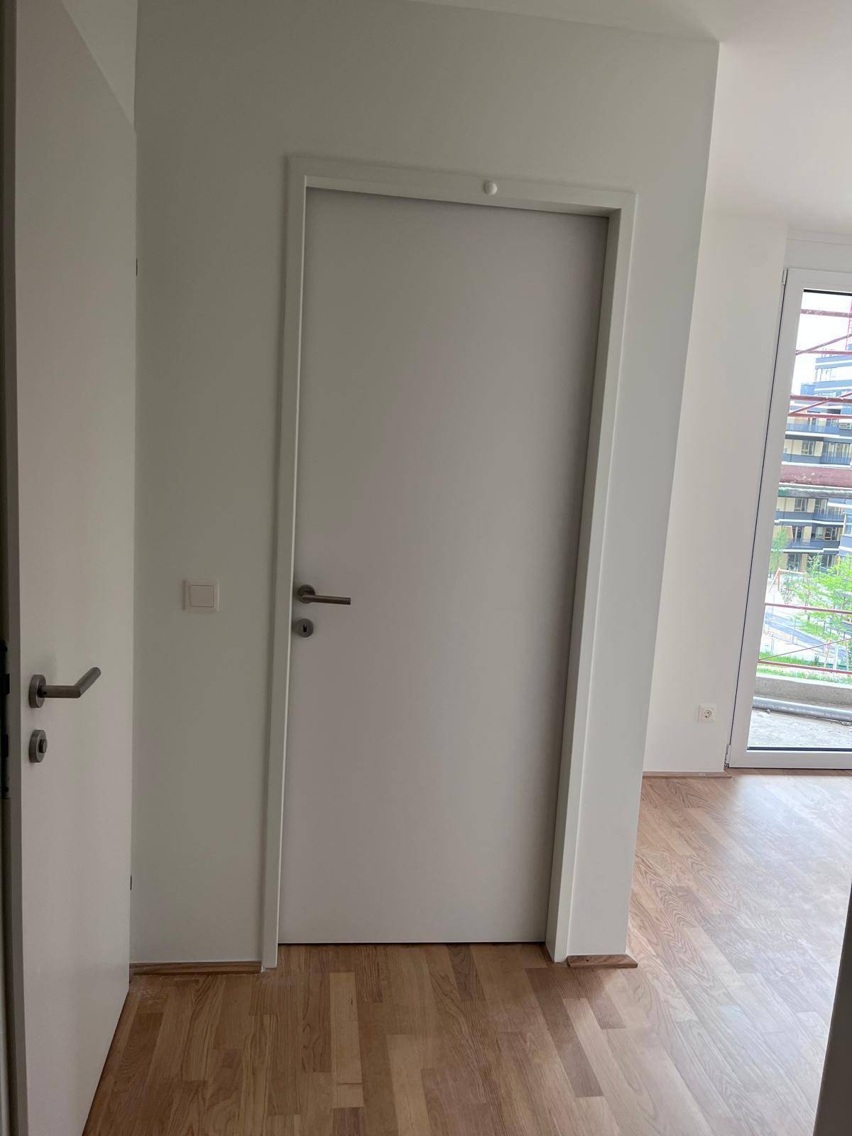 Heller Flurbereich mit zwei weißen Türen und Zugang zu einem weiteren Raum mit Tageslicht.