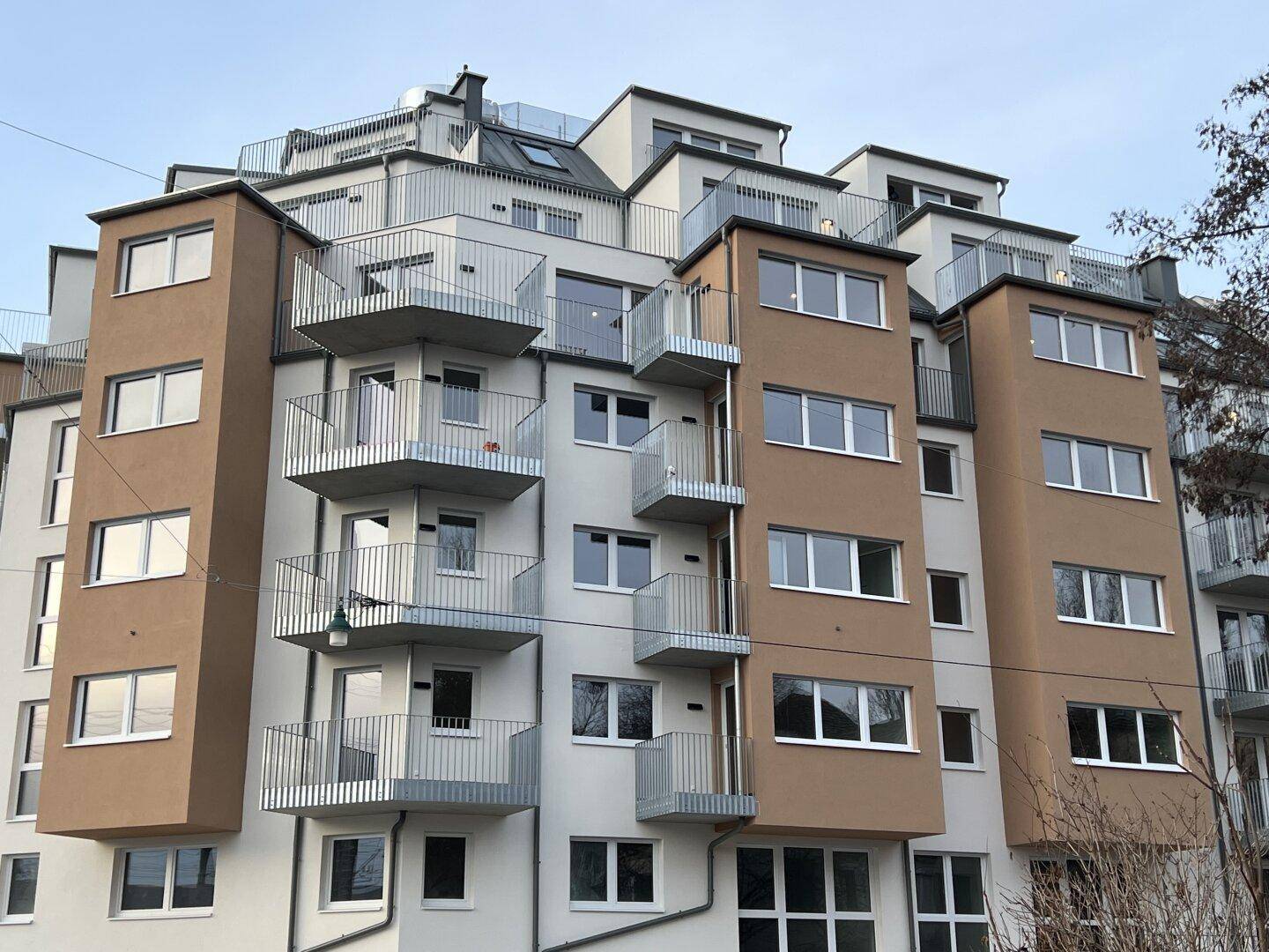 Moderne Wohnhausfassade mit zahlreichen Balkonen und großen Fenstern in städtischer Umgebung.