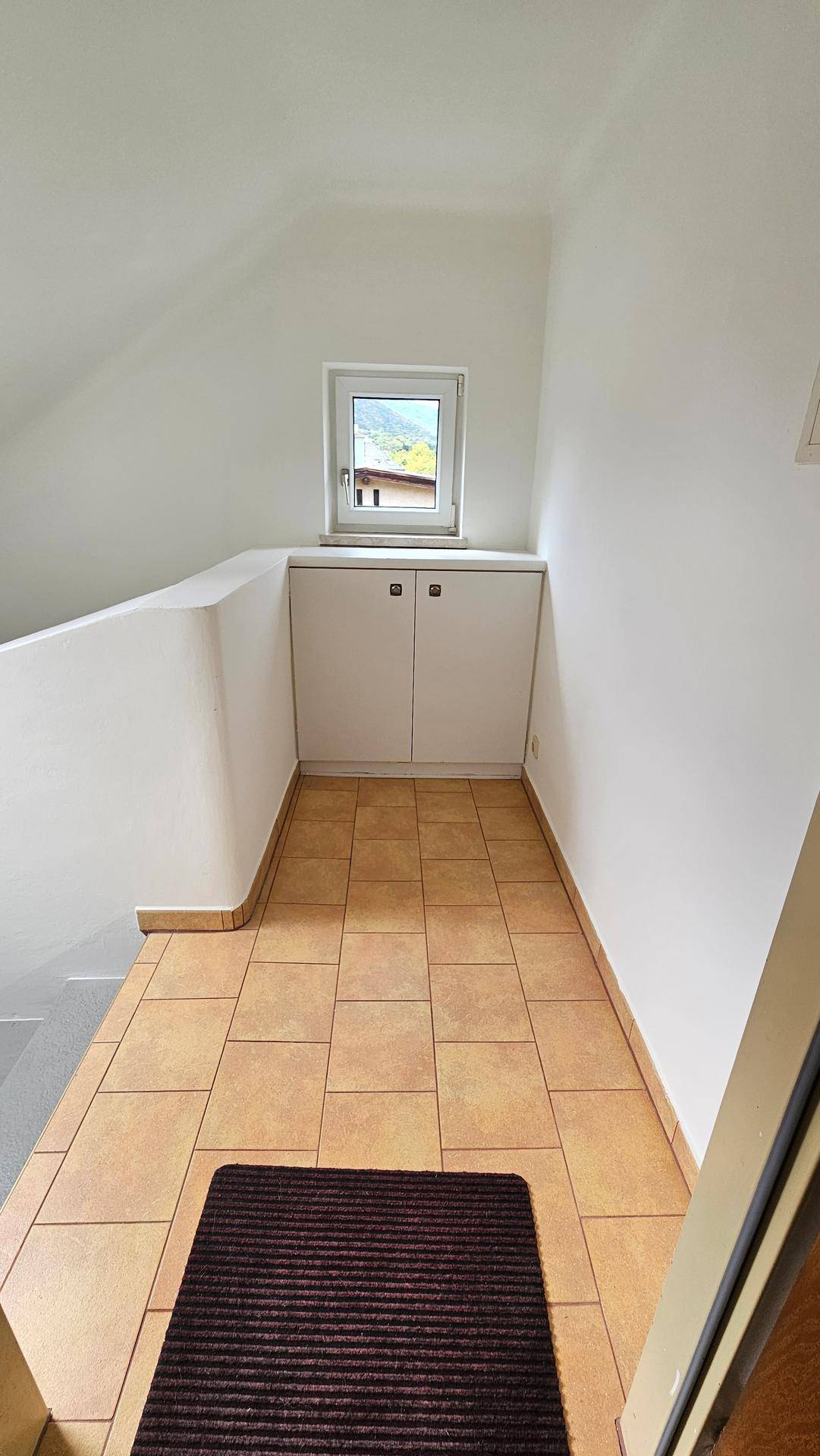 Heller Flur mit Fliesenboden, Einbauschrank und kleinem Fenster.