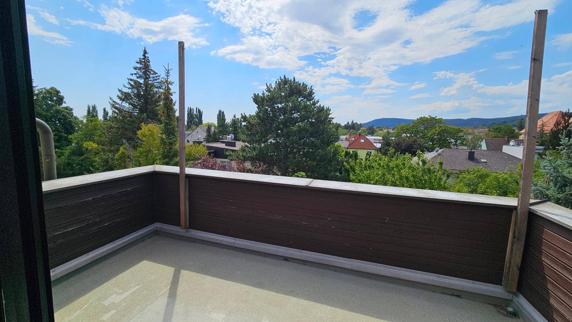 Sonniger Terrassenbereich mit Holzzaun und weitem Blick über die umliegende Landschaft.
