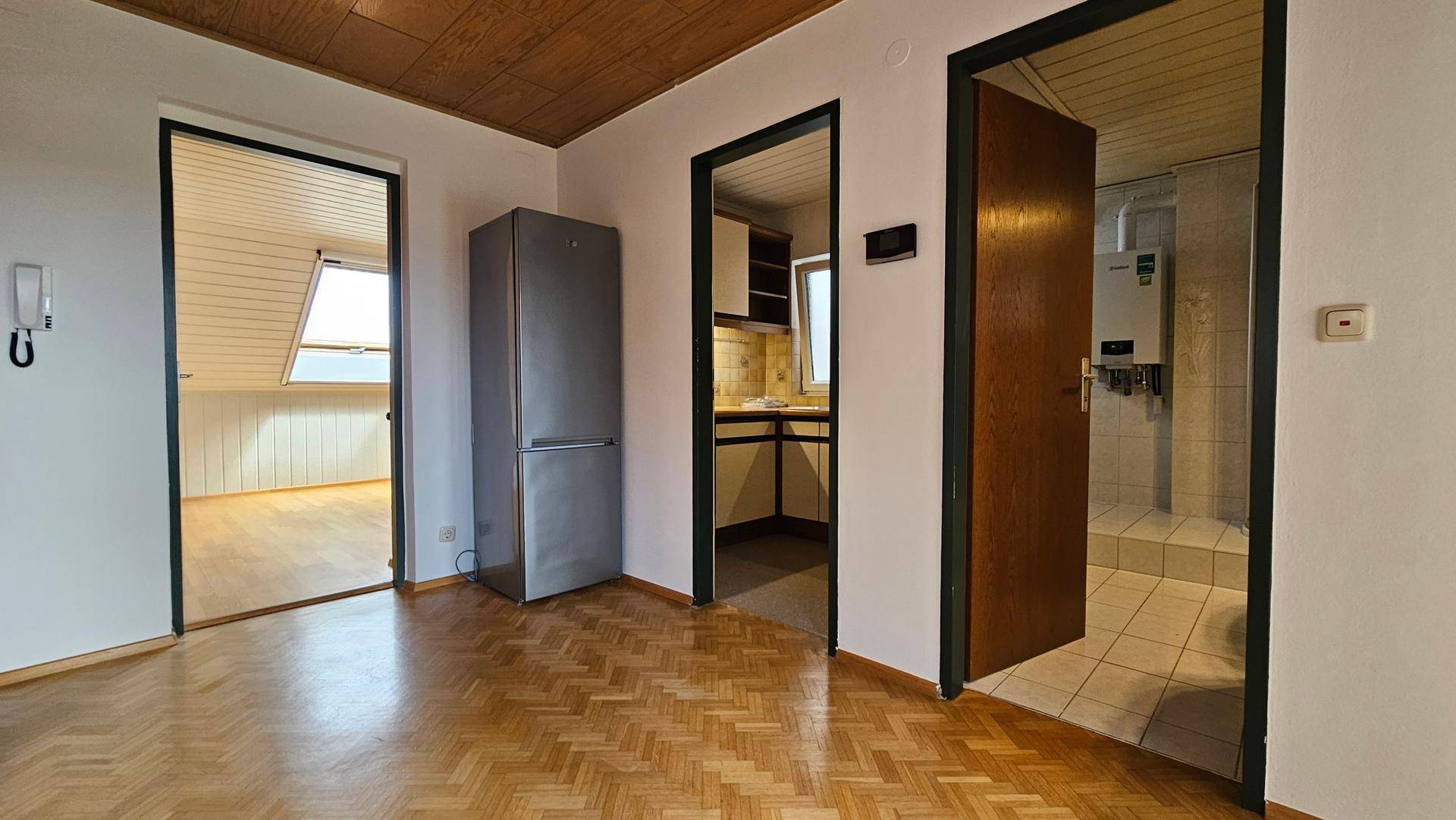 Übergangsbereich mit Parkettboden, Kühlschrank und Blick in Küche und Bad.