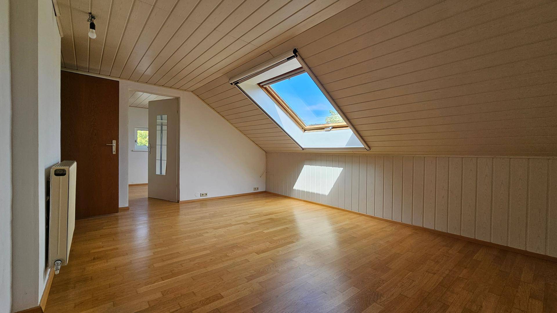 Geräumiger Dachgeschossraum mit Holzdecke, Parkettboden und viel natürlichem Licht.