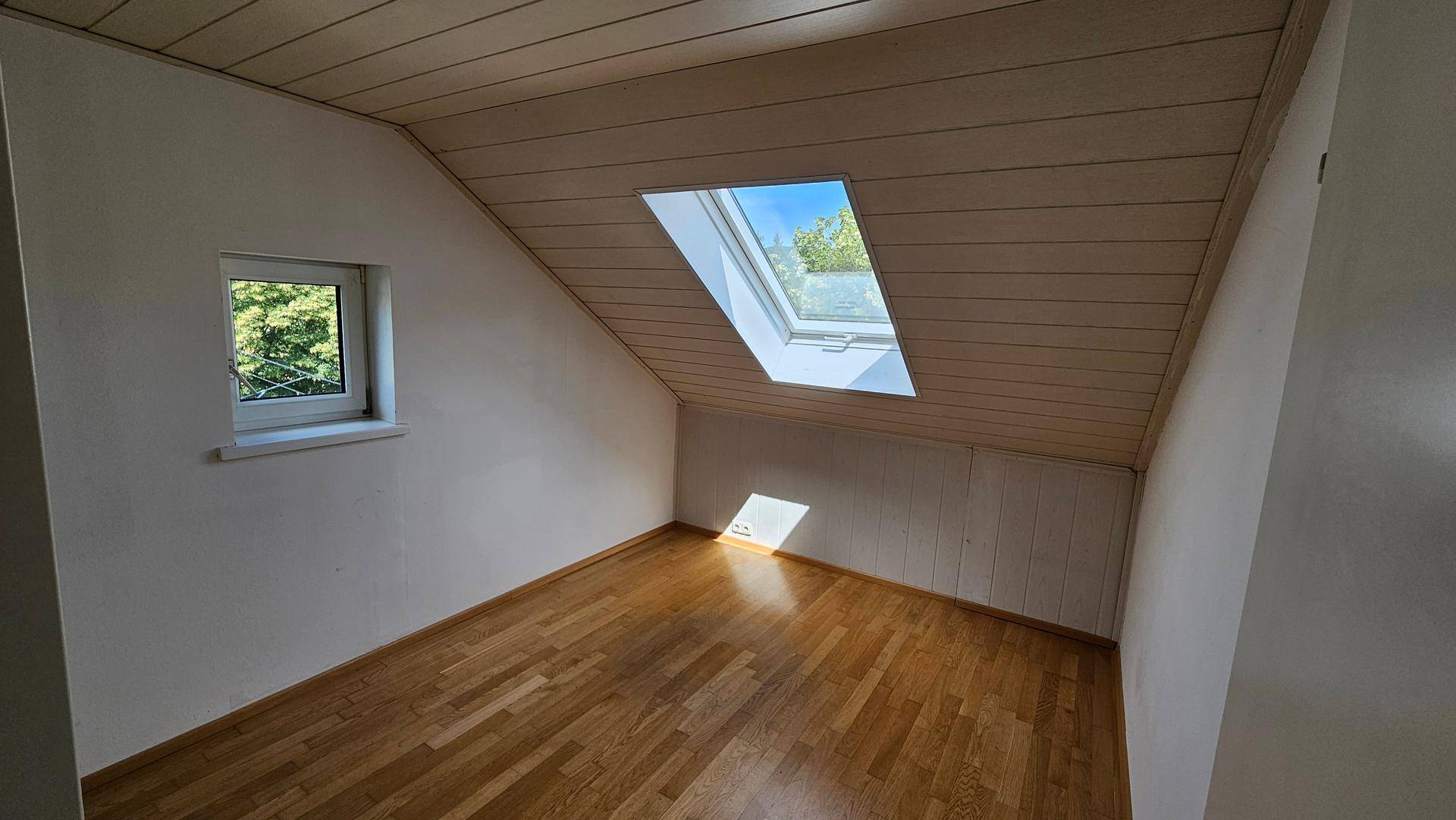 Helles Schlafzimmer im Dachgeschoss mit Holzdecke, Parkettboden und Dachfenster.