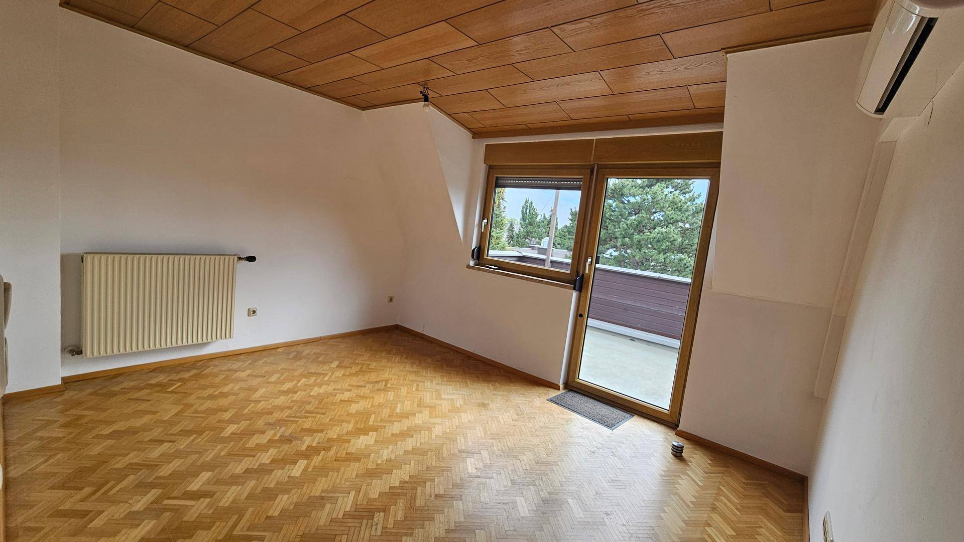 Heller Wohnraum mit Parkettboden, Holzdecke und Zugang zur Außenterrasse.
