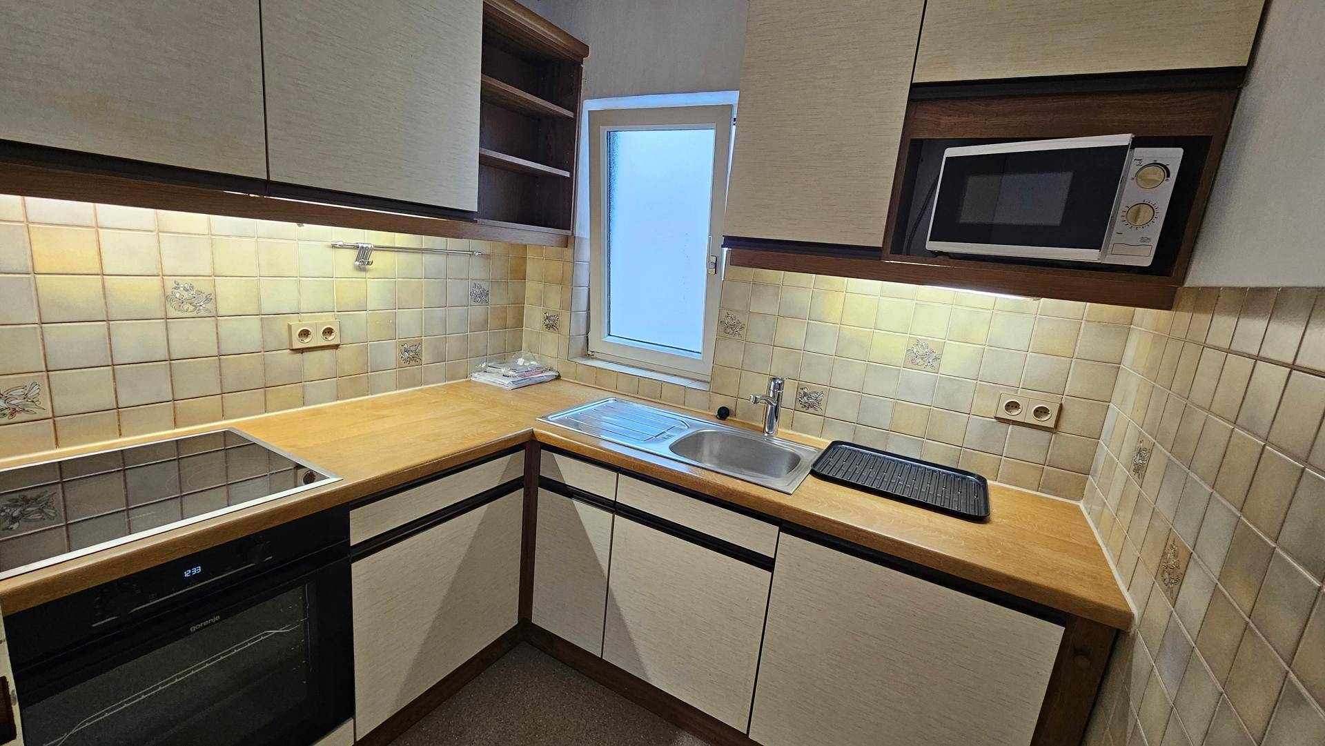 Kleine Einbauküche mit Holztheke, Fliesenrückwand und integrierten Geräten.
