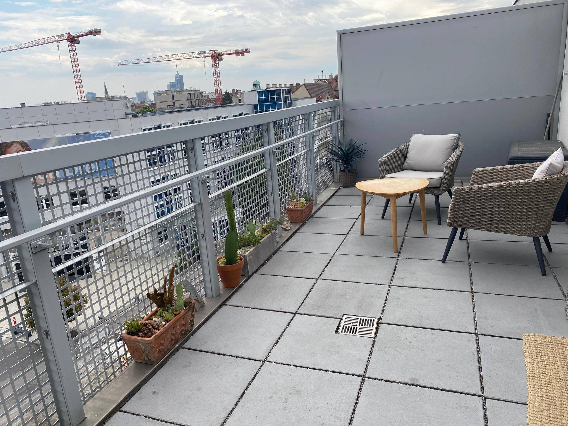 Balkon mit Sitzgelegenheiten, Pflanzen und Blick auf die Stadt mit Baukranen.