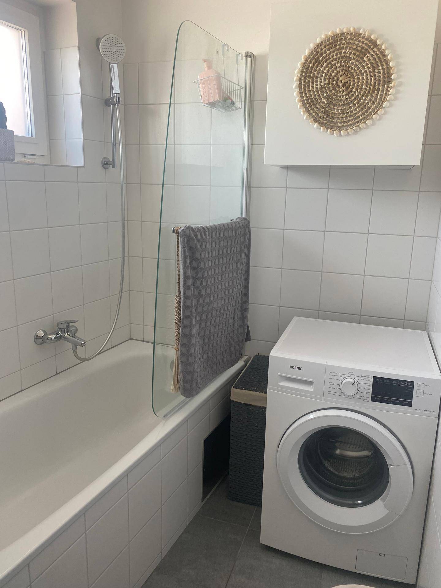 Badezimmer mit Badewanne, Duschvorrichtung, Glasabtrennung und Waschmaschine.