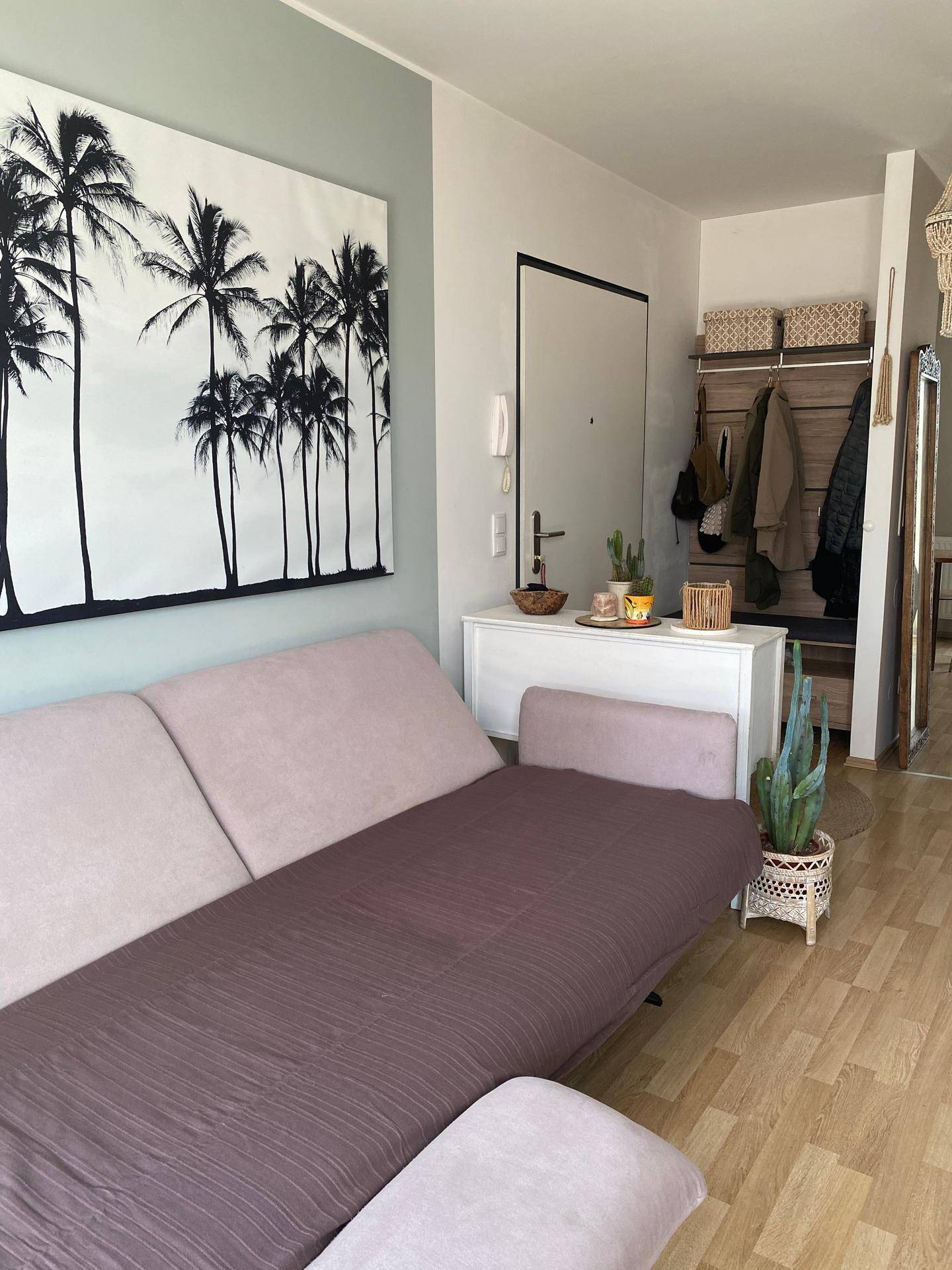 Gemütliches Wohnzimmer mit Sofa, großem Palmenbild und Blick auf den Eingangsbereich.