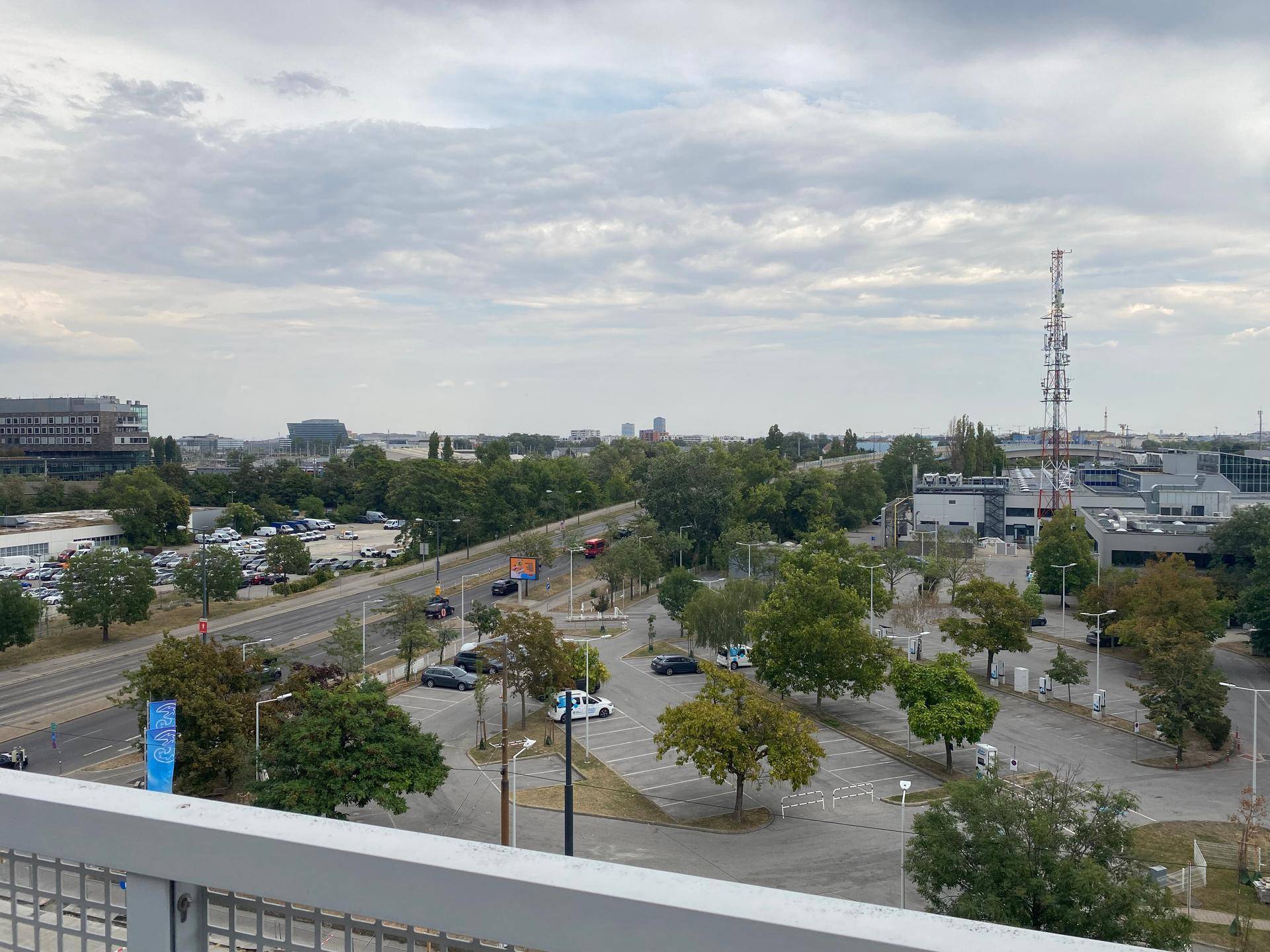 Weitläufiger Blick über die städtische Umgebung mit Straßen, Parkplätzen und viel Grün.