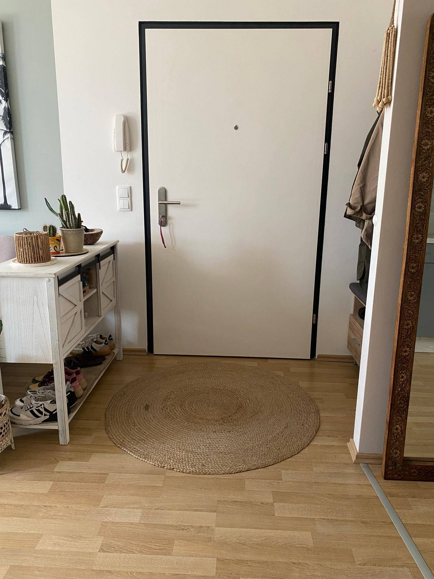 Eingangsbereich mit heller Tür, Schuhschrank und einem runden Jute-Teppich.