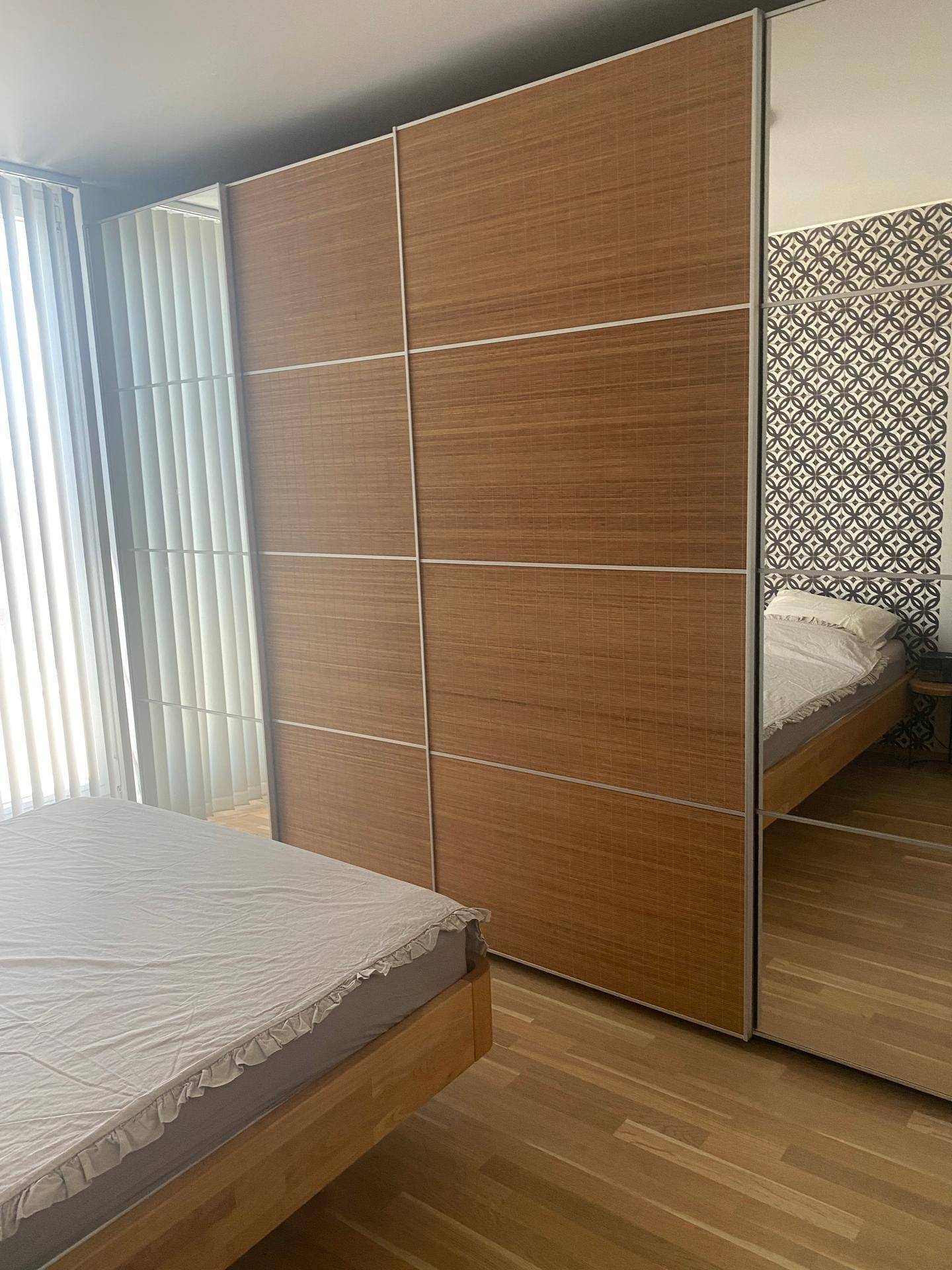 Schlafzimmer mit großen Schiebetürenschränken, teils aus Holz, teils verspiegelt.