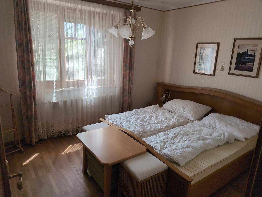 Schlafzimmer mit Doppelbett, Holzboden und hellen Vorhängen, die eine gemütliche Atmosphäre bieten.
