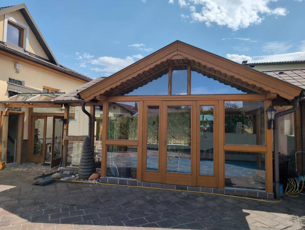 Außenansicht des Wintergartens oder Poolhauses mit großen Glasflächen und Holzelementen im Sonnenlicht.