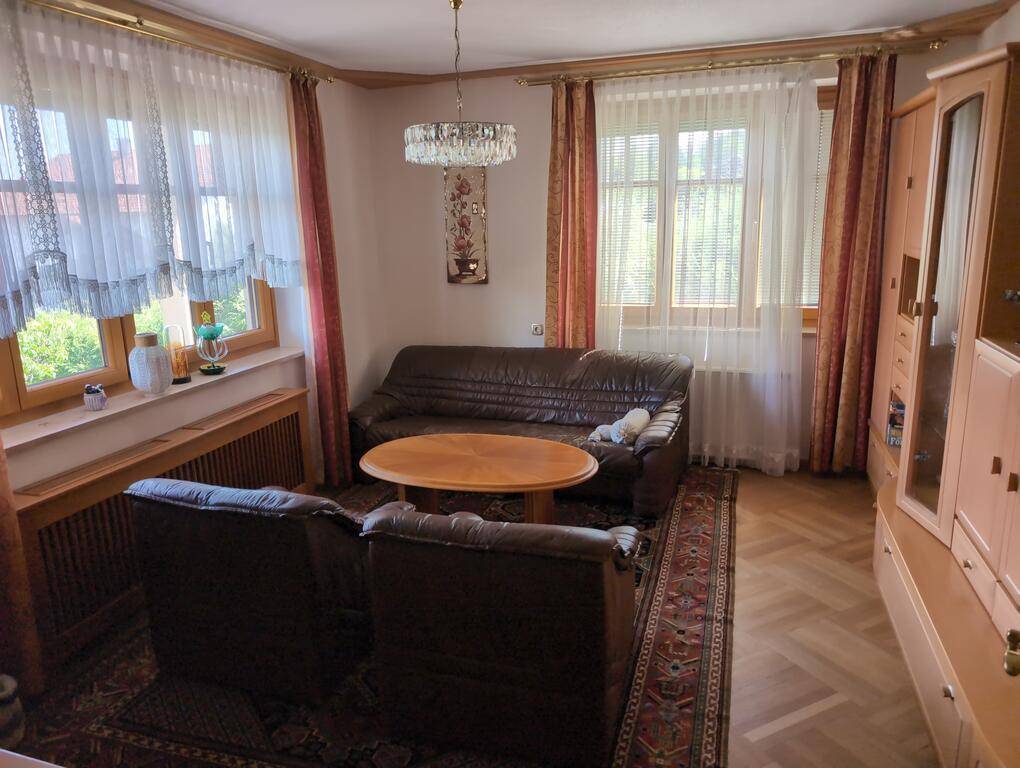 Wohnzimmer mit bequemen Ledersofas, Parkettboden und großen Fenstern, die viel Licht hereinlassen.