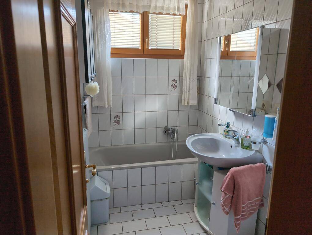 Helles Badezimmer mit Badewanne, Waschbecken und weißen Fliesen, ausgestattet mit einem Fenster.