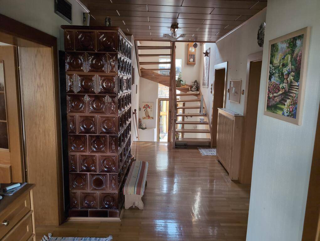 Geräumiger Flur mit traditionellem Kachelofen, Holztreppe und Holzbalkendecke, die eine warme Atmosphäre schafft.