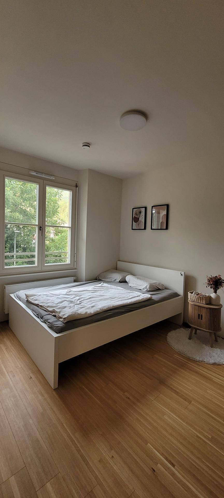 Schlafzimmer mit Holzboden, weißem Bett und Blick ins Grüne.