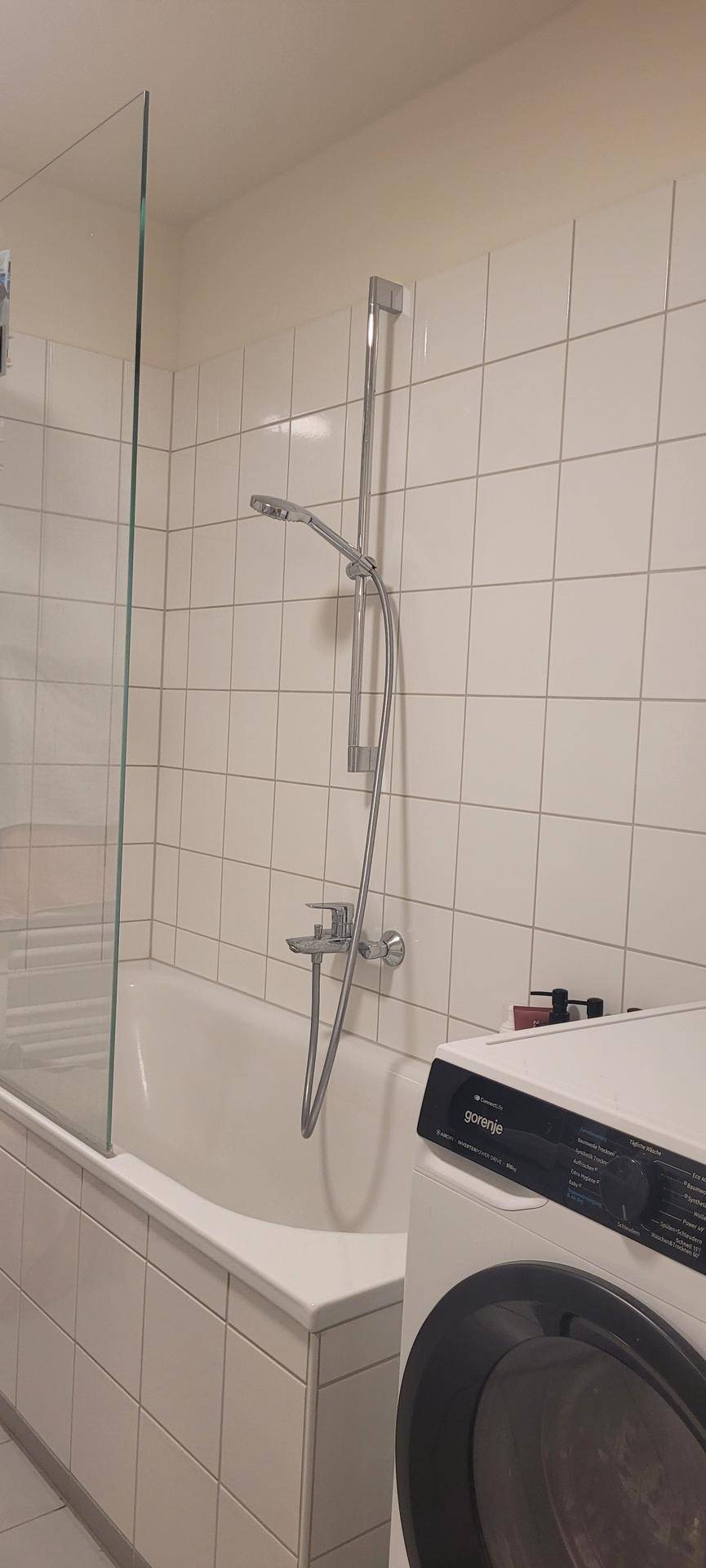 Badezimmer mit Badewanne, Duschfunktion und integrierter Waschmaschine.