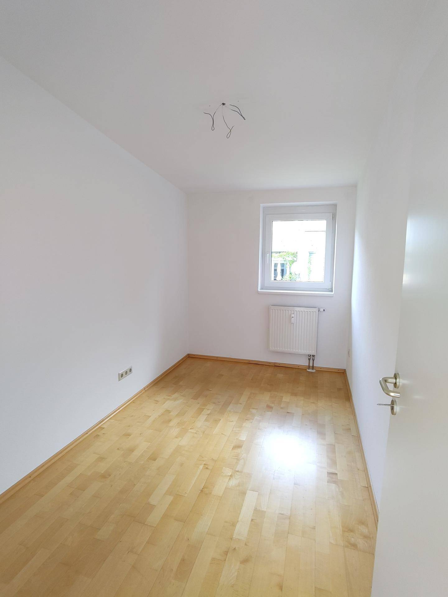 Leeres Schlafzimmer mit hellem Parkettboden und weiß gestrichenen Wänden.