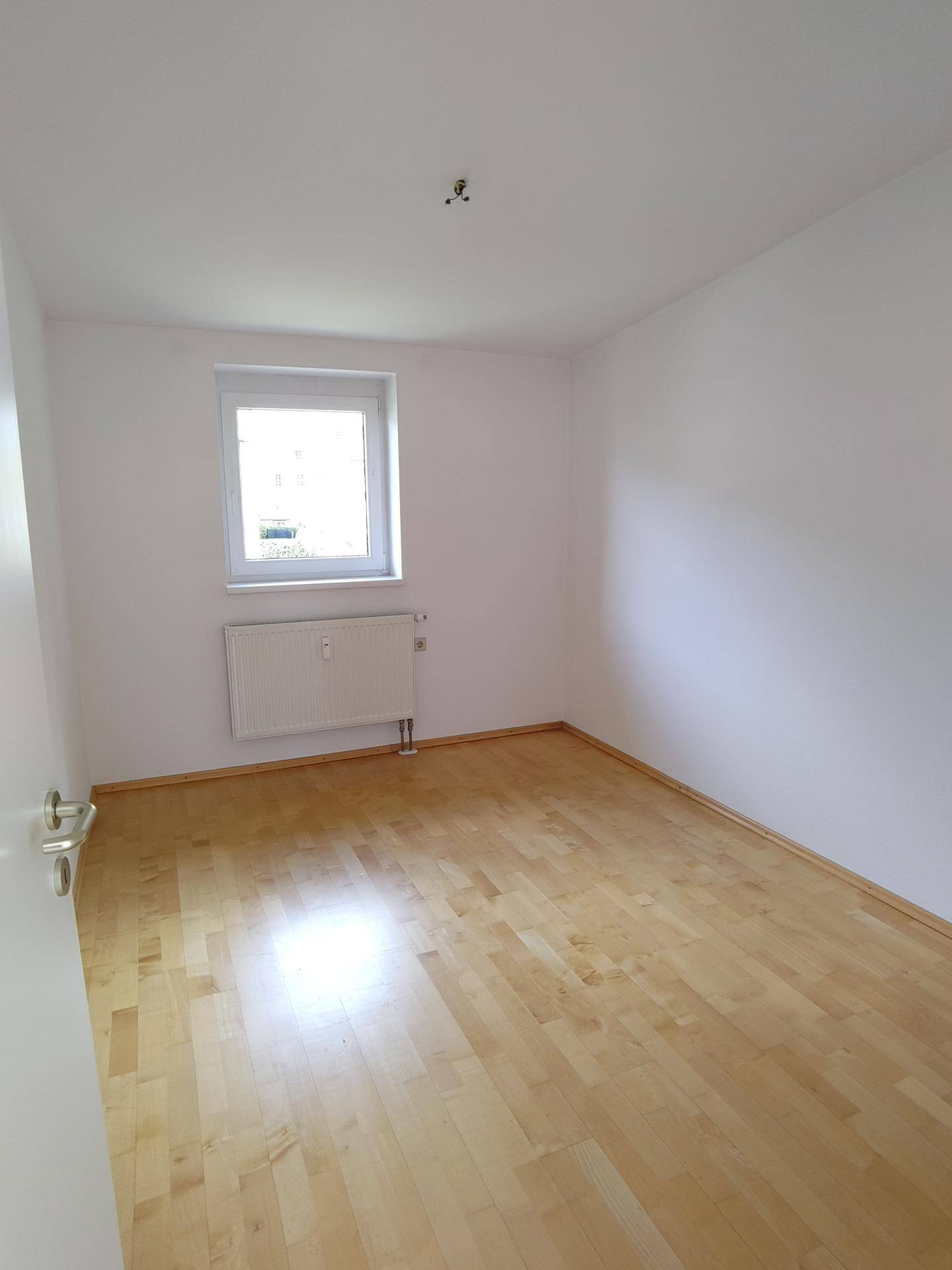 Helles Schlafzimmer mit Parkettboden und einem Fenster.