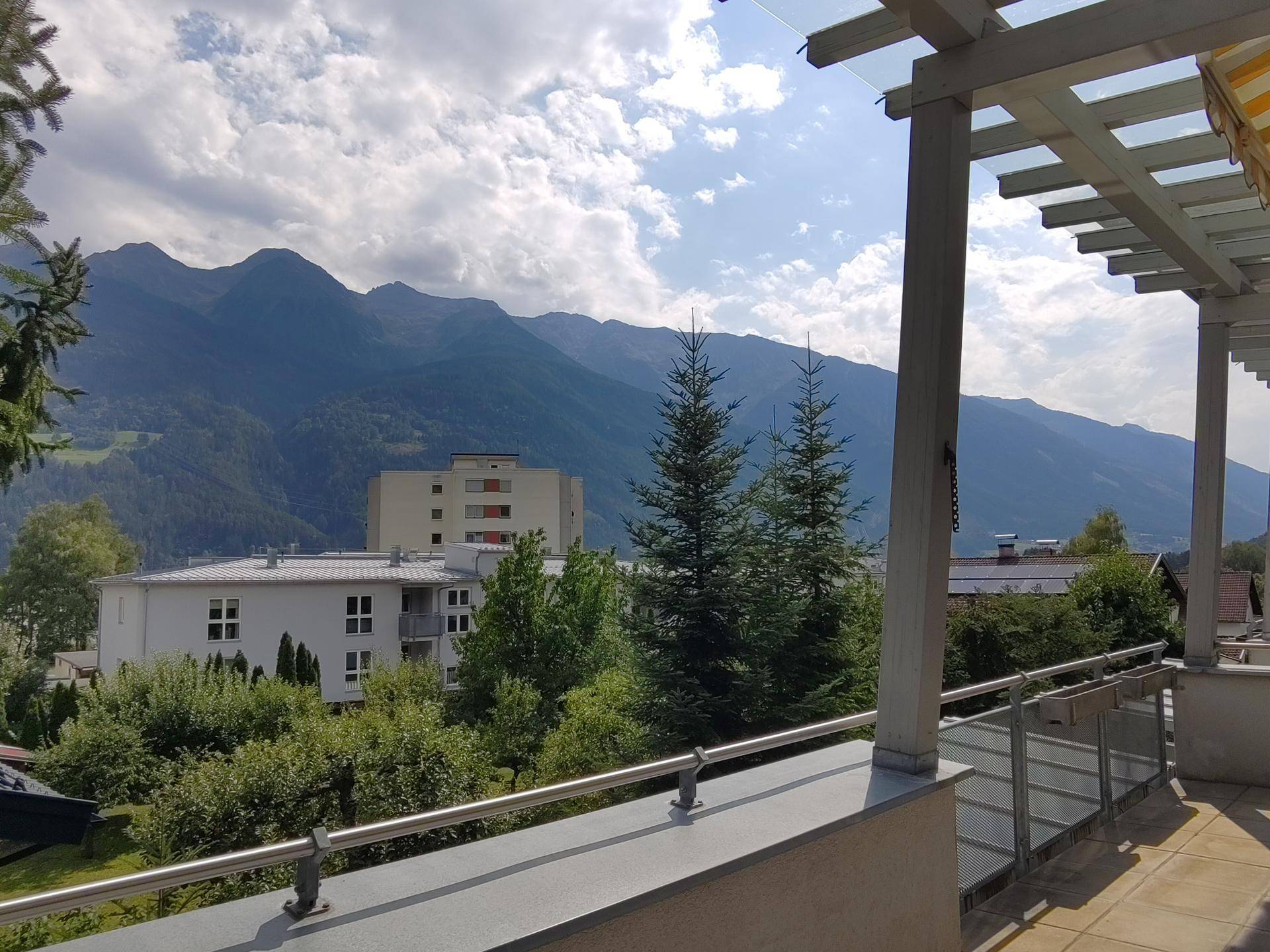 Panoramablick von der Terrasse auf die umliegende Berglandschaft und Gebäude.