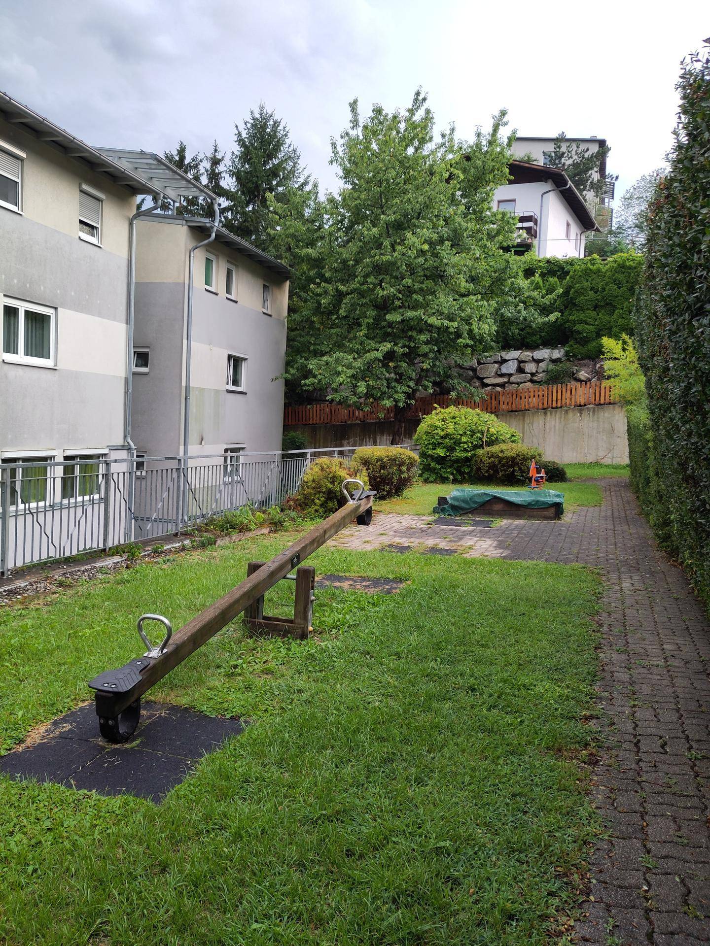 Spielbereich im Freien mit einer Wippe, Sandkasten und Grünflächen.