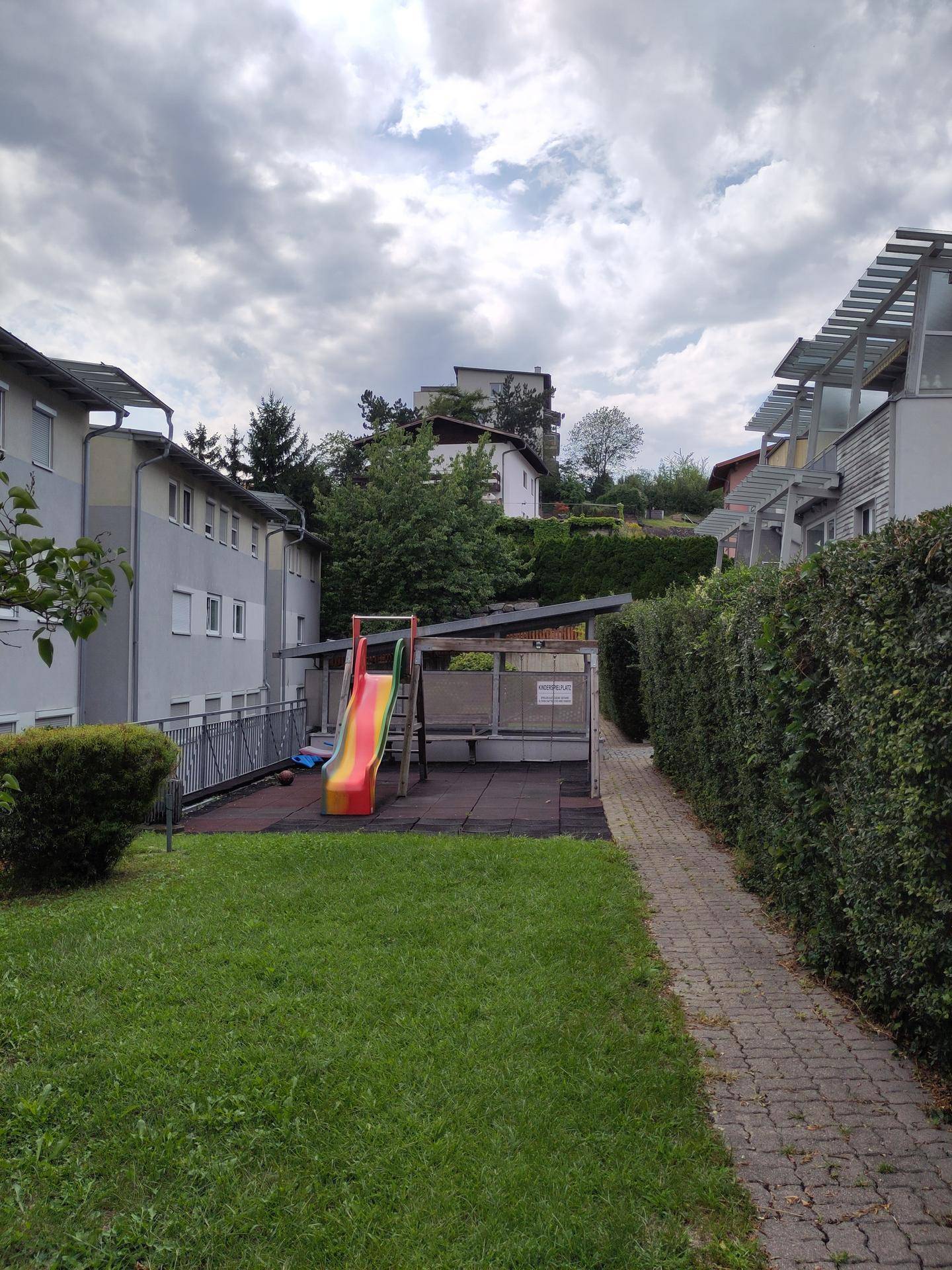 Kinderspielplatz im Freien mit einer Rutsche, umgeben von Rasen und Hecken.