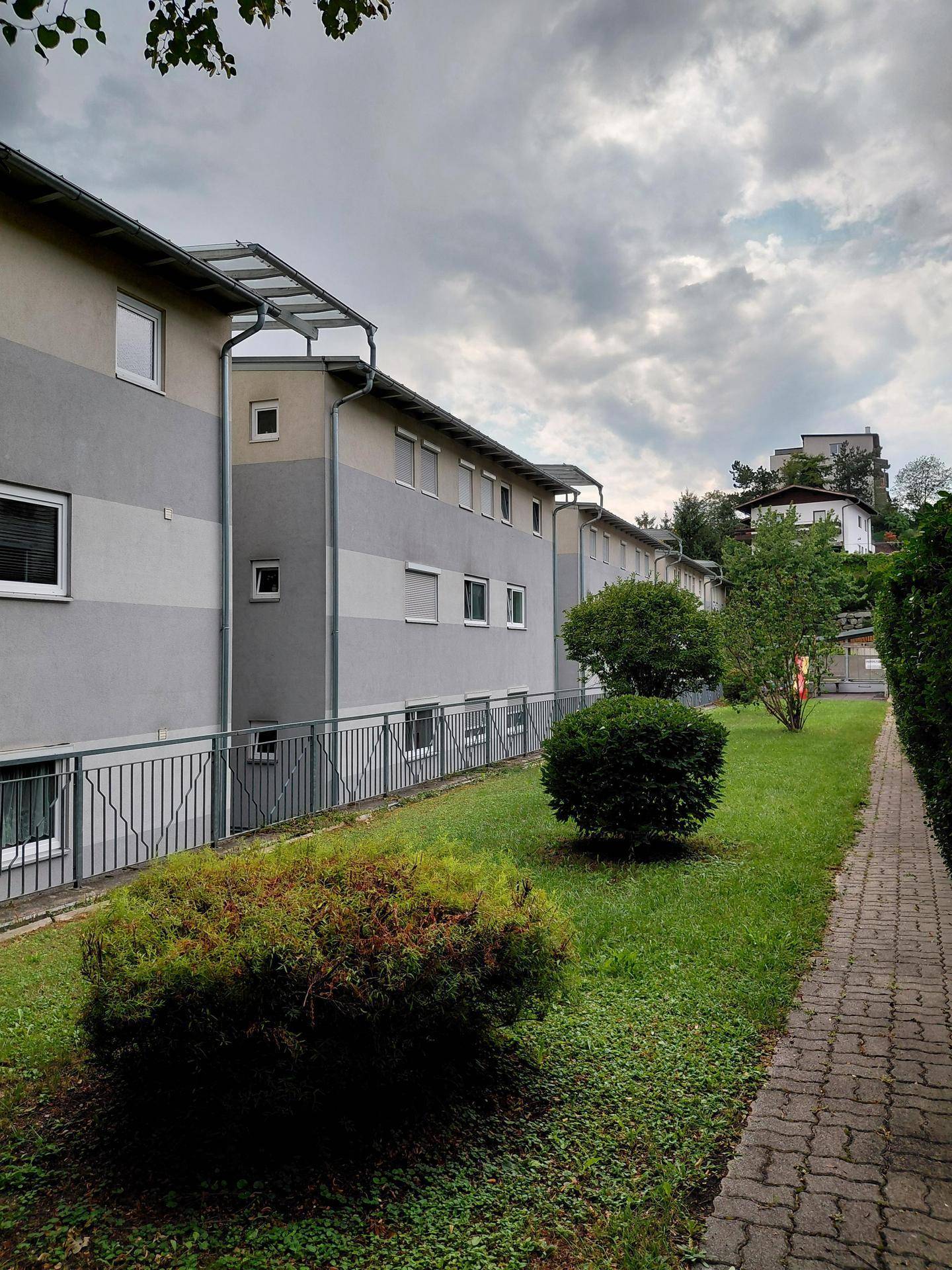Seitenansicht des Gebäudes mit gepflegtem Rasen, Hecken und einem Gehweg.