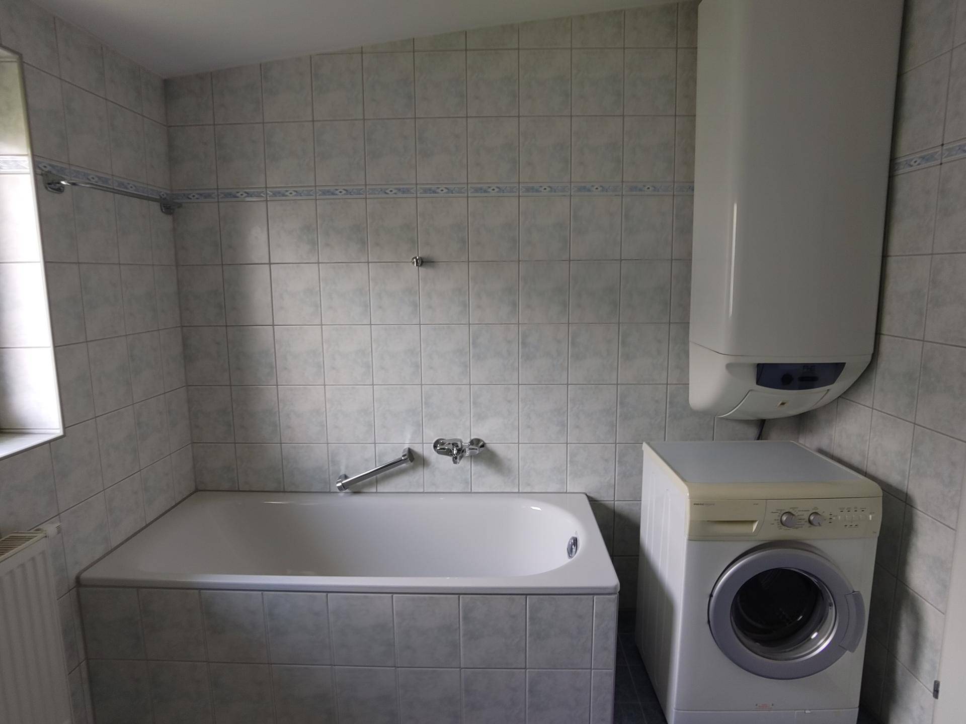 Badezimmer mit Badewanne, Waschmaschine und Warmwasserboiler.