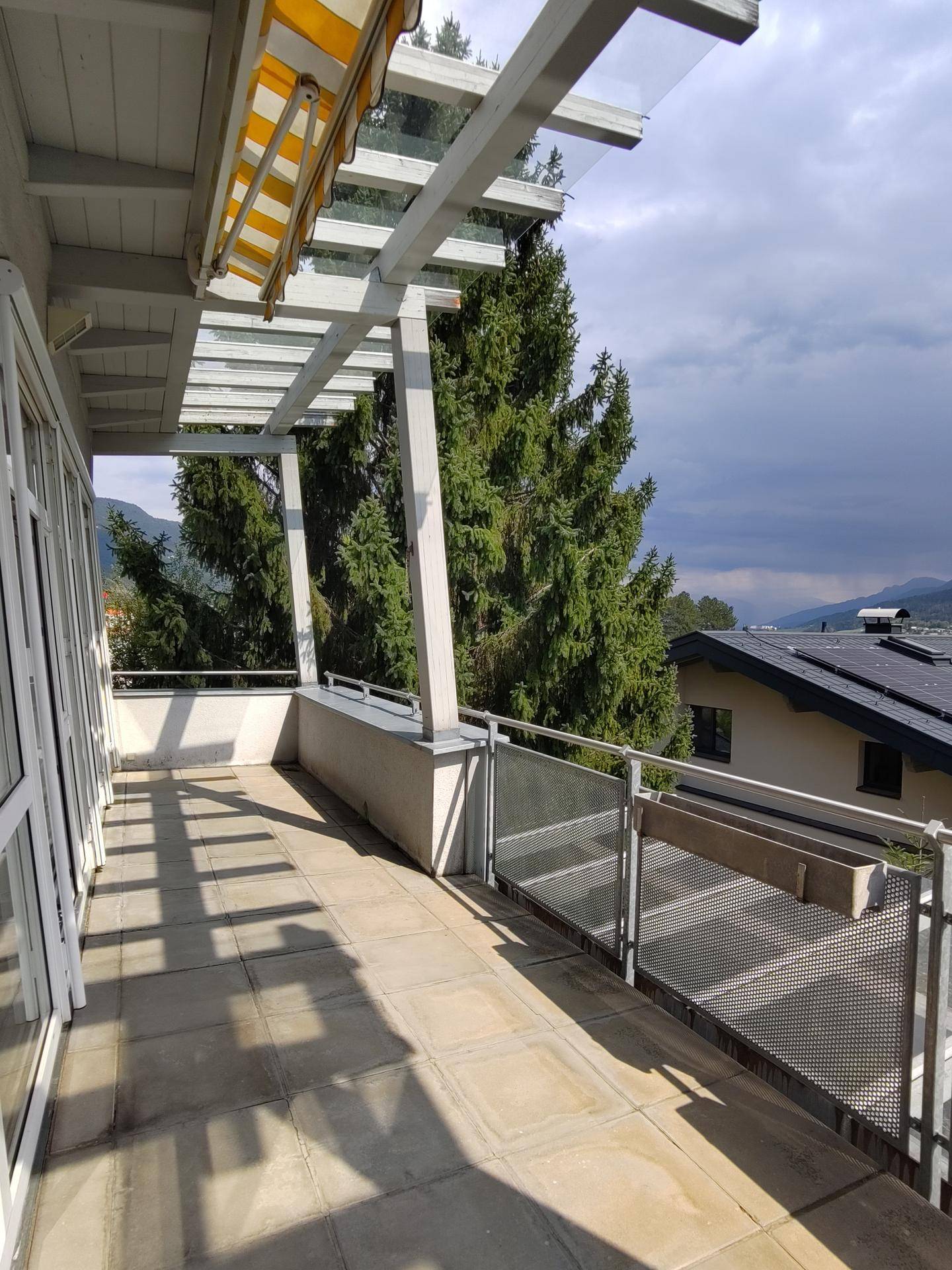 Weitläufige Terrasse mit Fliesenboden, Metallgeländer und Blick ins Grüne.