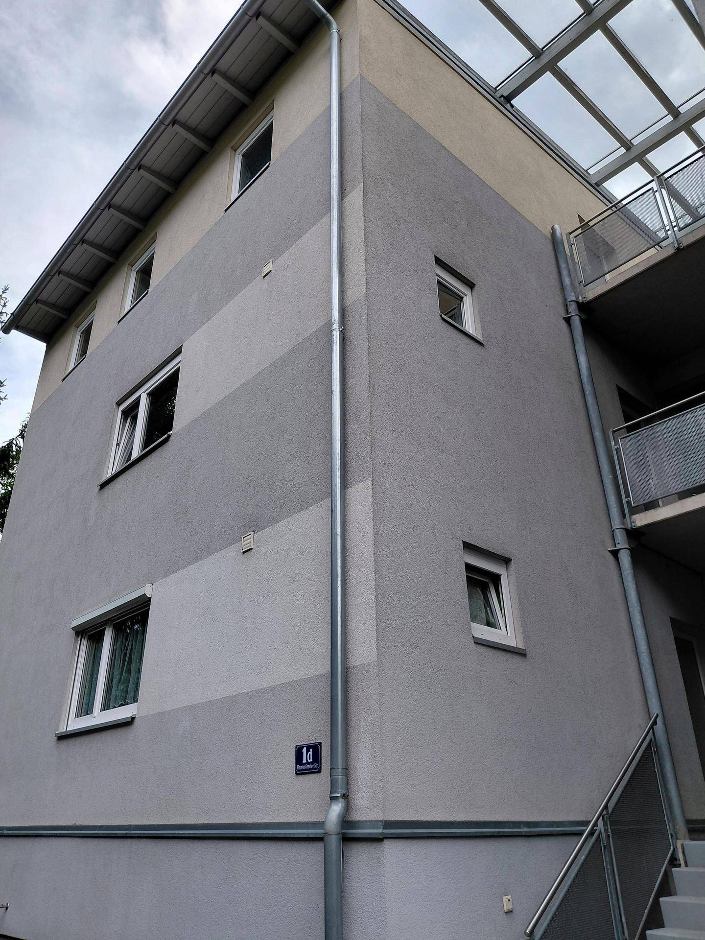 Moderne Gebäudefassade mit grauen und beigen Streifen und mehreren Fenstern.